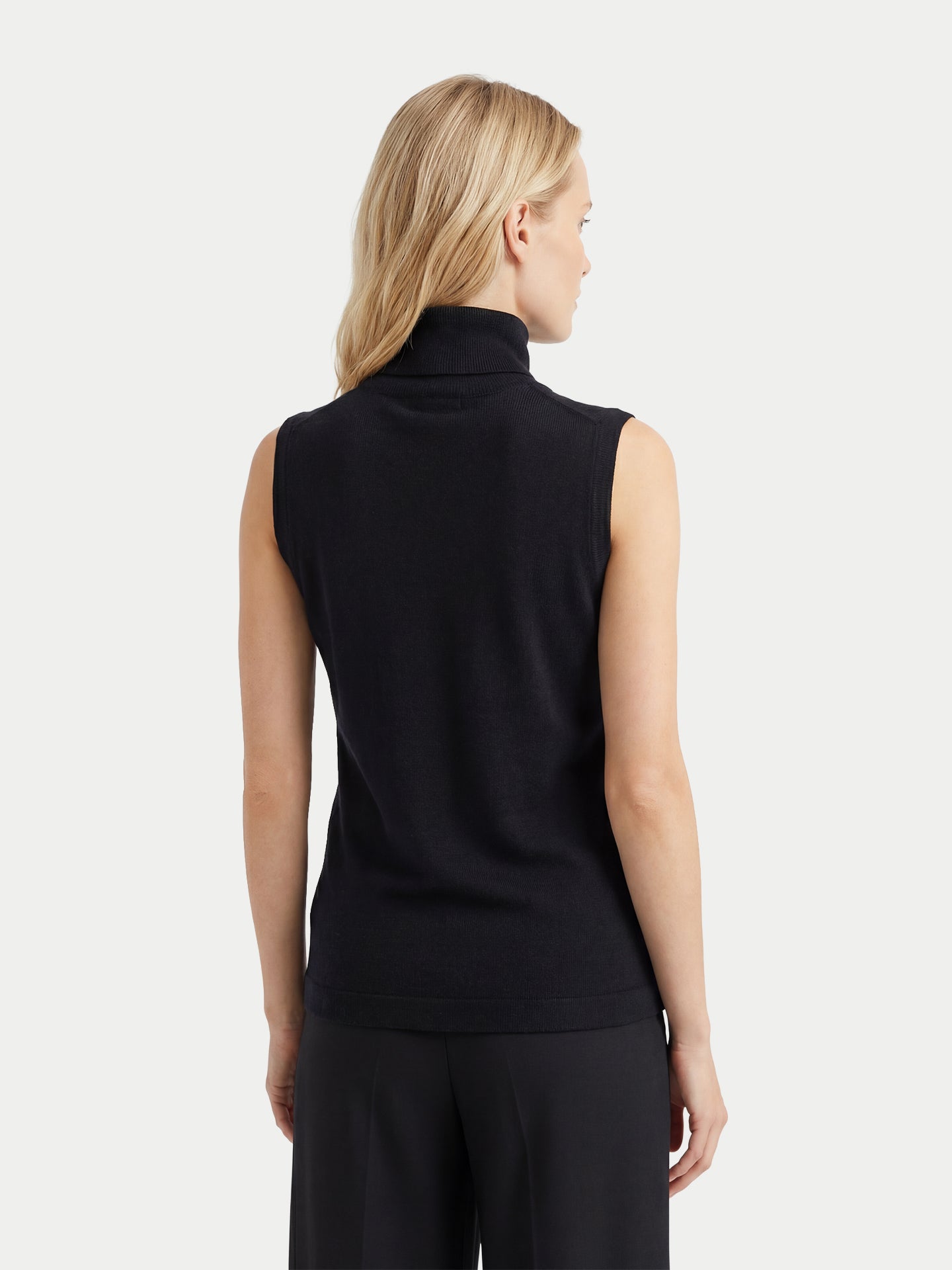 Vue de dos d'une femme portant un haut en cachemire noir sans manches à col roulé assorti à un pantalon, sur un fond gris clair. #color_noir
