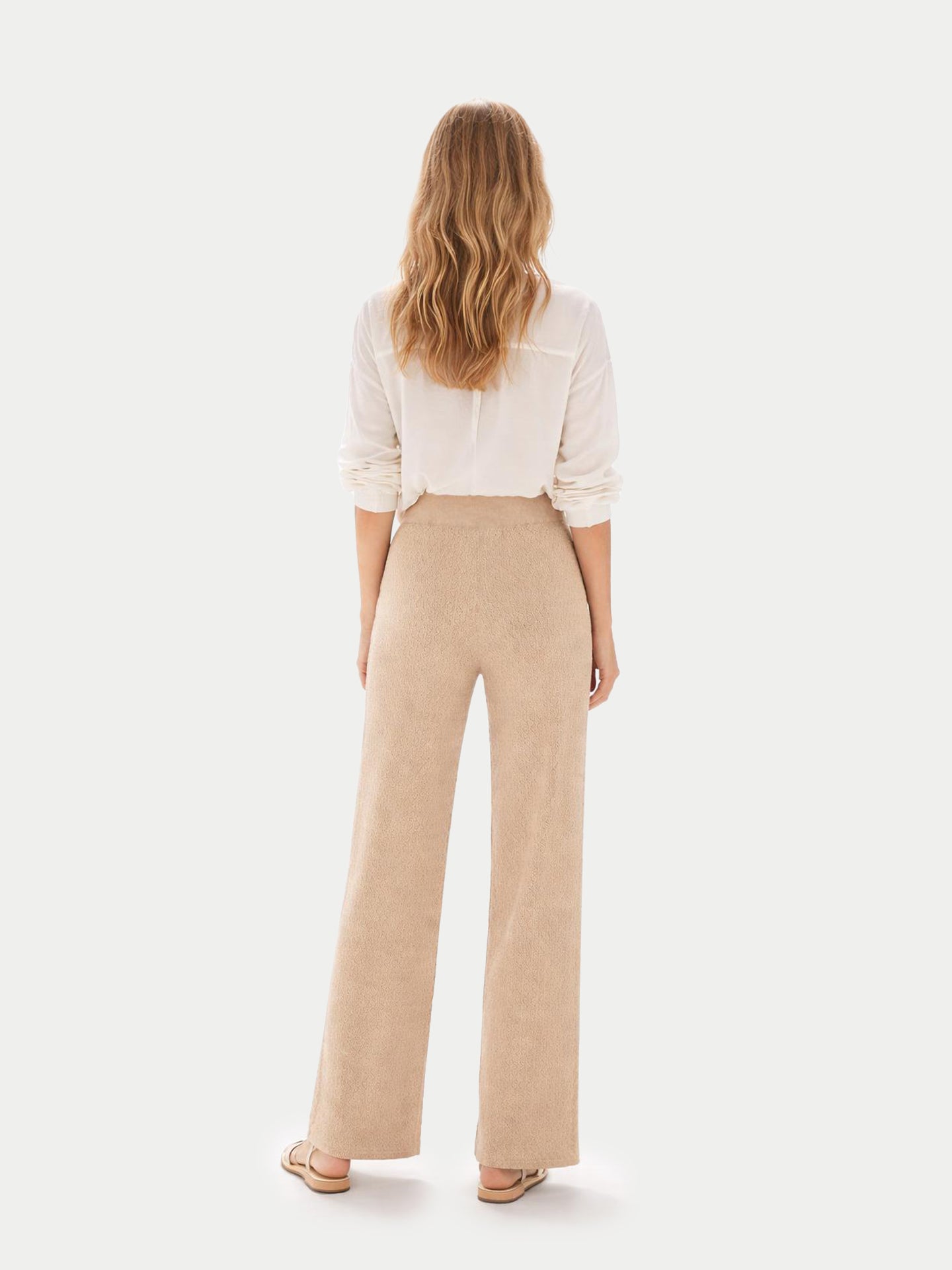 Vue de dos d'une femme portant une chemise blanche et un pantalon large en maille côtelée beige sur fond gris clair. #color_beige
