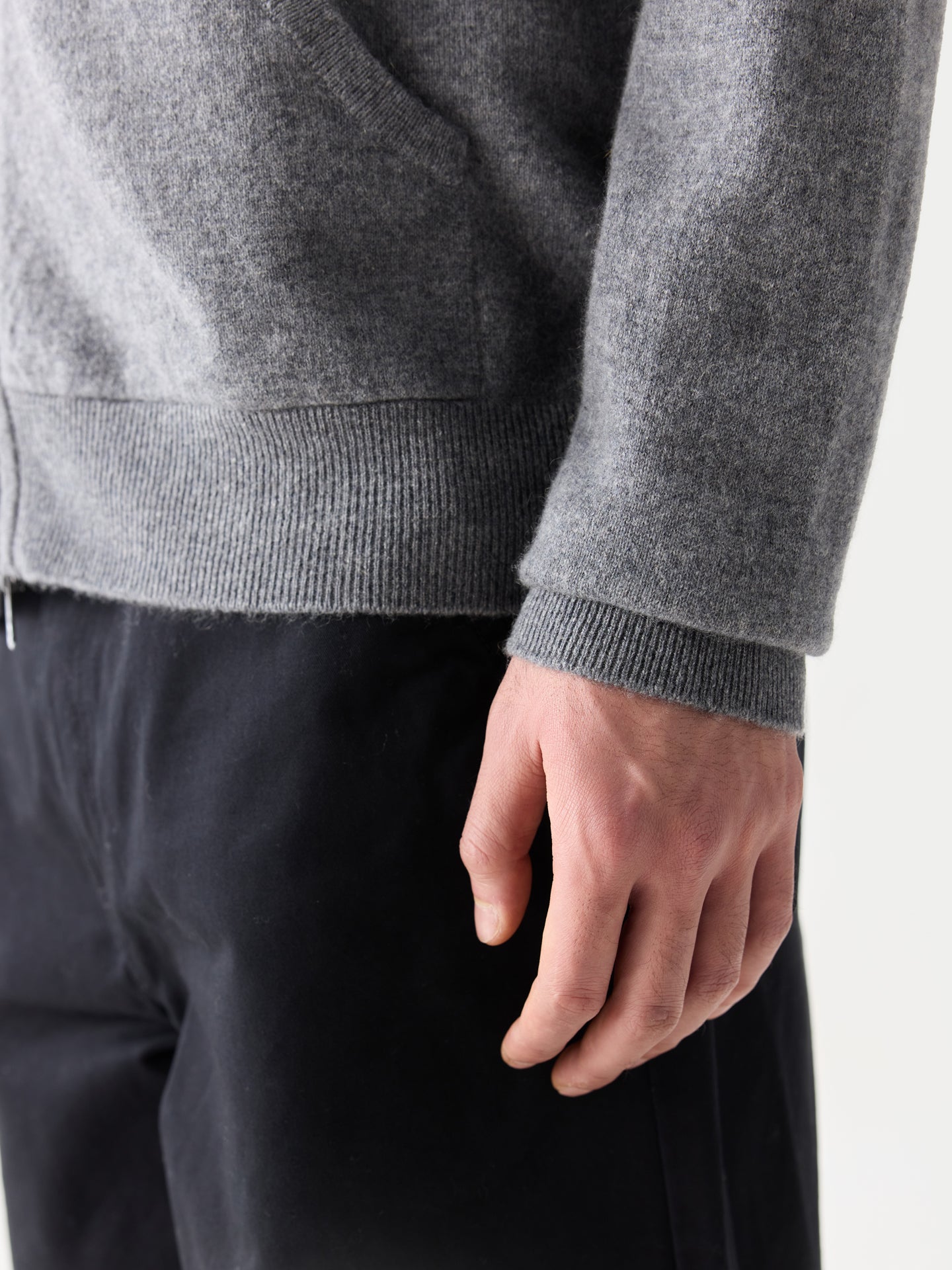 Gros plan latéral sur la manche d'un sweat à capuche gris et un pantalon noir sur fond gris clair. #color_gris-foncé