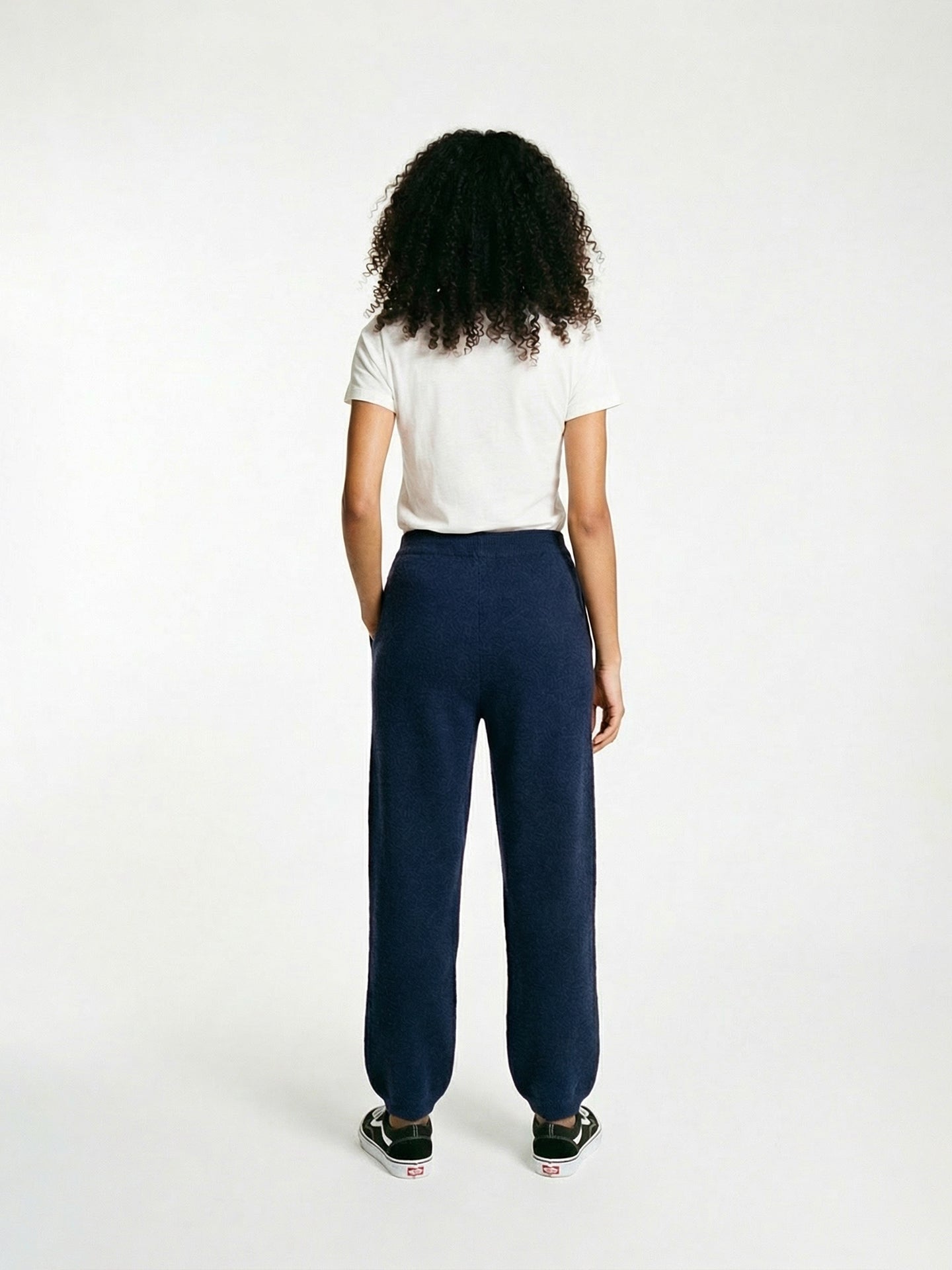 Vue de dos d'une femme portant un pantalon de jogging bleu marine et une chemise blanche sur fond gris clair. #color_india-ink