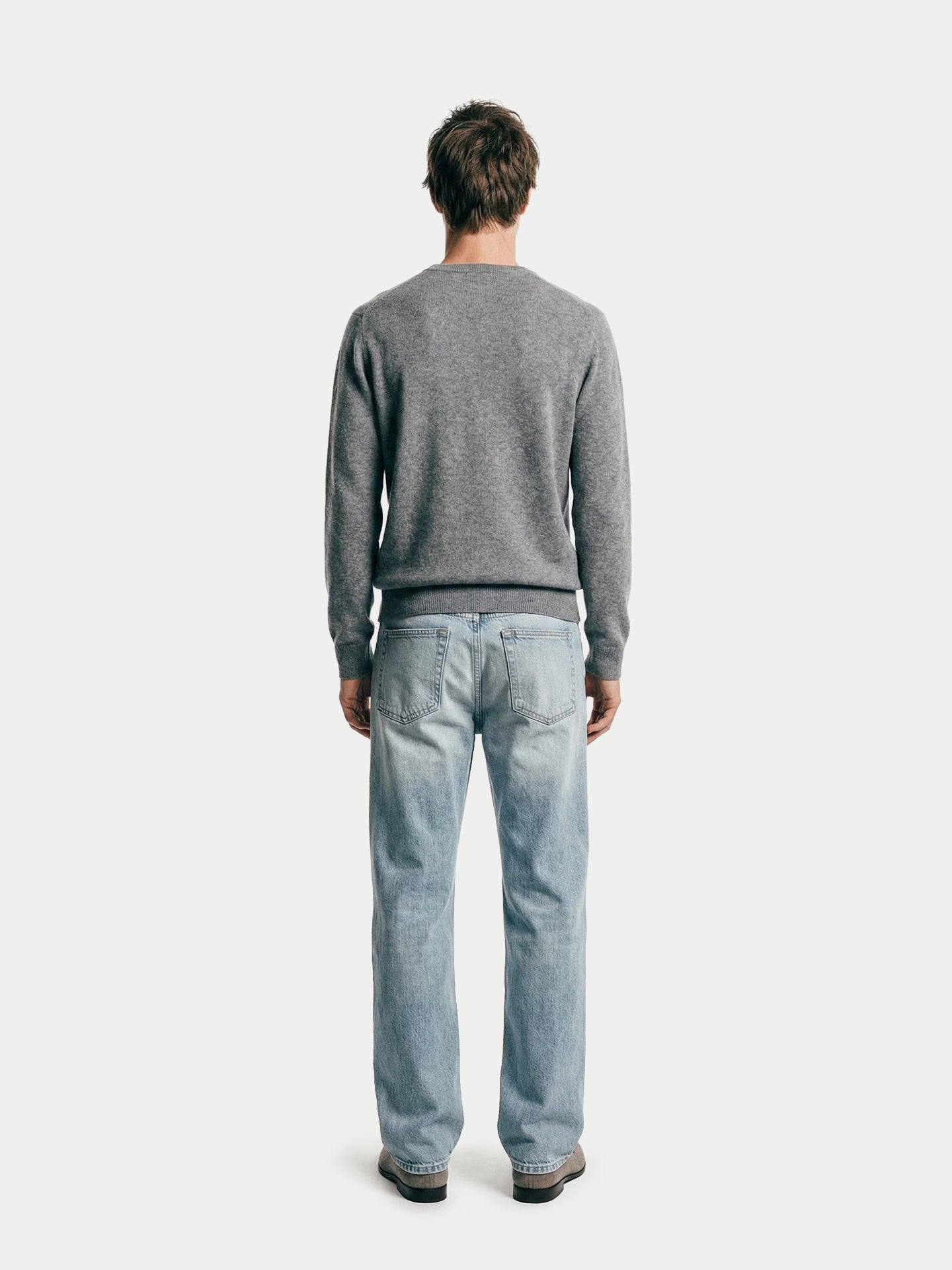 Vue de dos d'un homme portant un pull gris à col en V et un jean bleu sur fond gris clair. #color_gris-foncé