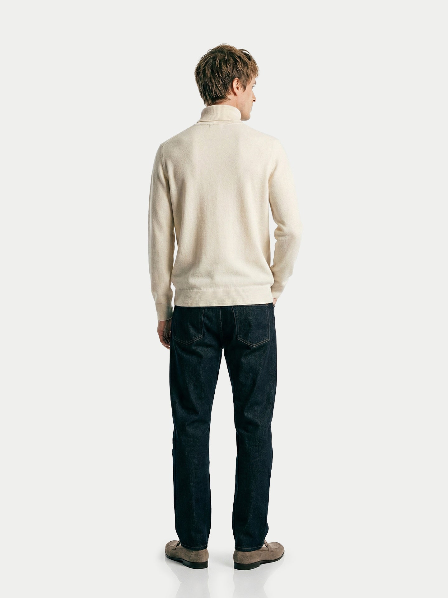 Vue de dos d'un homme portant un pull à col roulé blanc et un jean sur fond gris clair. #color_blanc-cassé