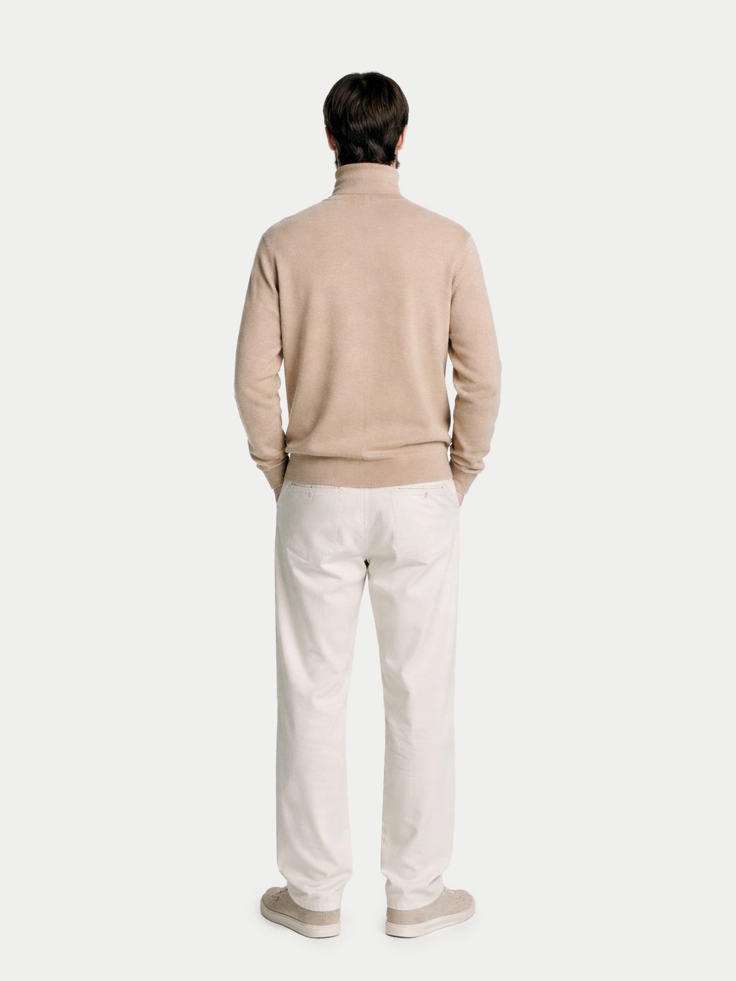 Vue de dos d'un homme portant un pull à col roulé beige et un pantalon blanc sur fond gris clair. #color_beige