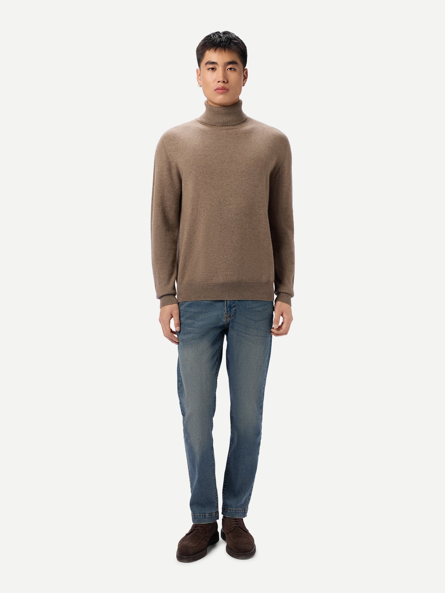 Vue de face d'un homme portant un pull à col roulé beige et un jean bleu sur fond gris clair. #color_taupe