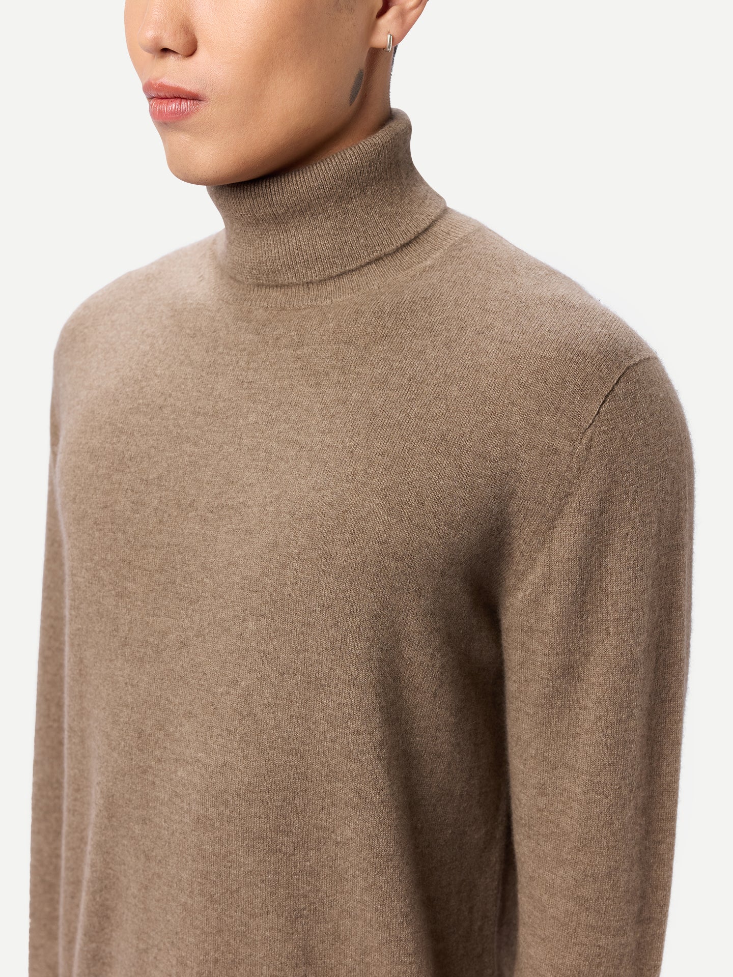 Gros plan de profil d'un homme portant un pull à col roulé beige sur fond gris clair. #color_taupe