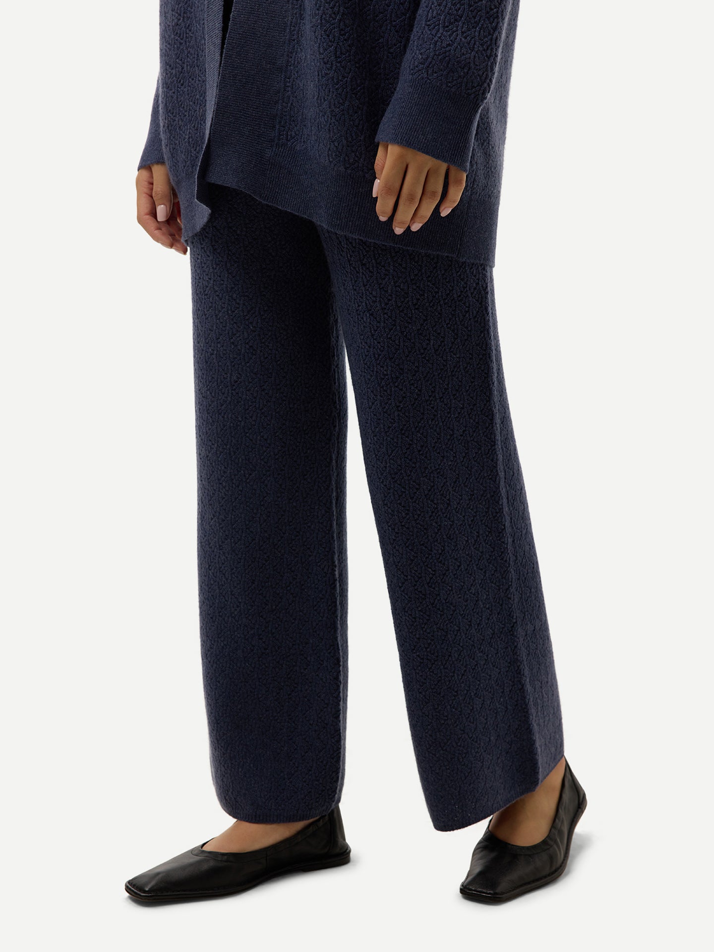 Gros plan sur une femme portant un pantalon large bleu côtelé et des ballerines noires, sur fond gris clair. #color_bleu-courrone