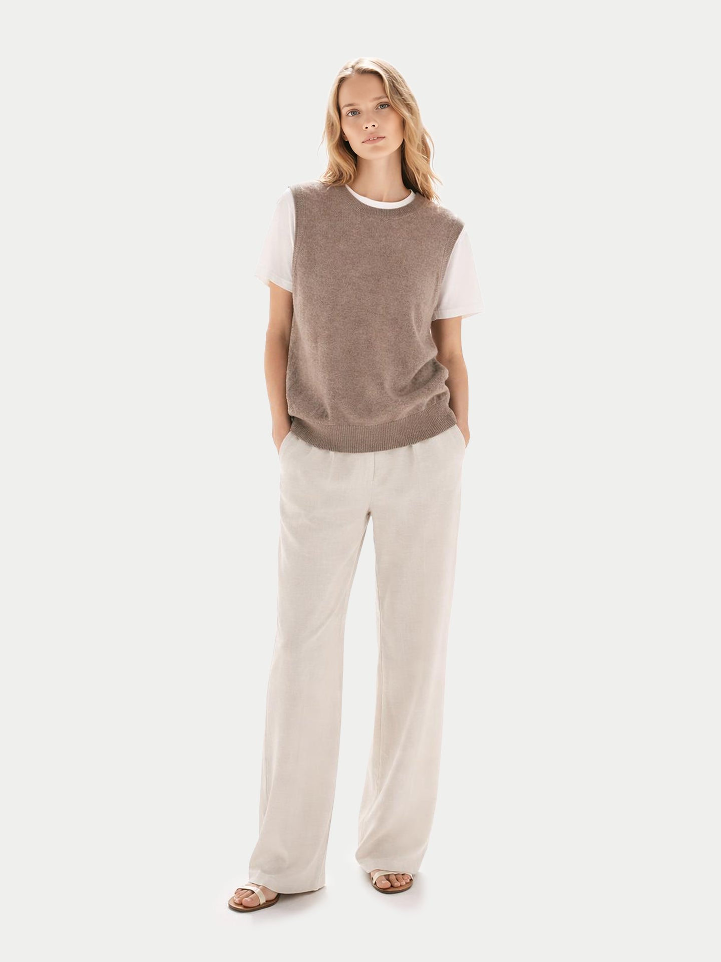Vue de face d'une femme portant un débardeur beige à col rond sur un t-shirt blanc et un pantalon blanc, sur fond gris clair. #color_taupe