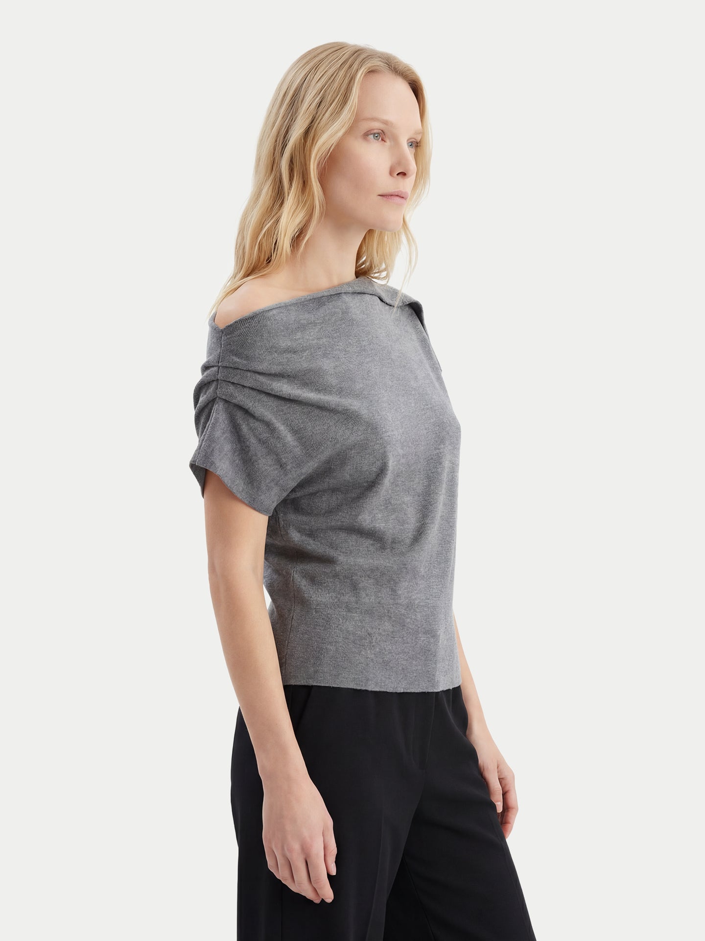 Gros plan latéral d'un haut en cachemire gris à manches courtes, col asymétrique et taille côtelée, et d'un pantalon noir sur fond gris clair.
#color_gris-pierre