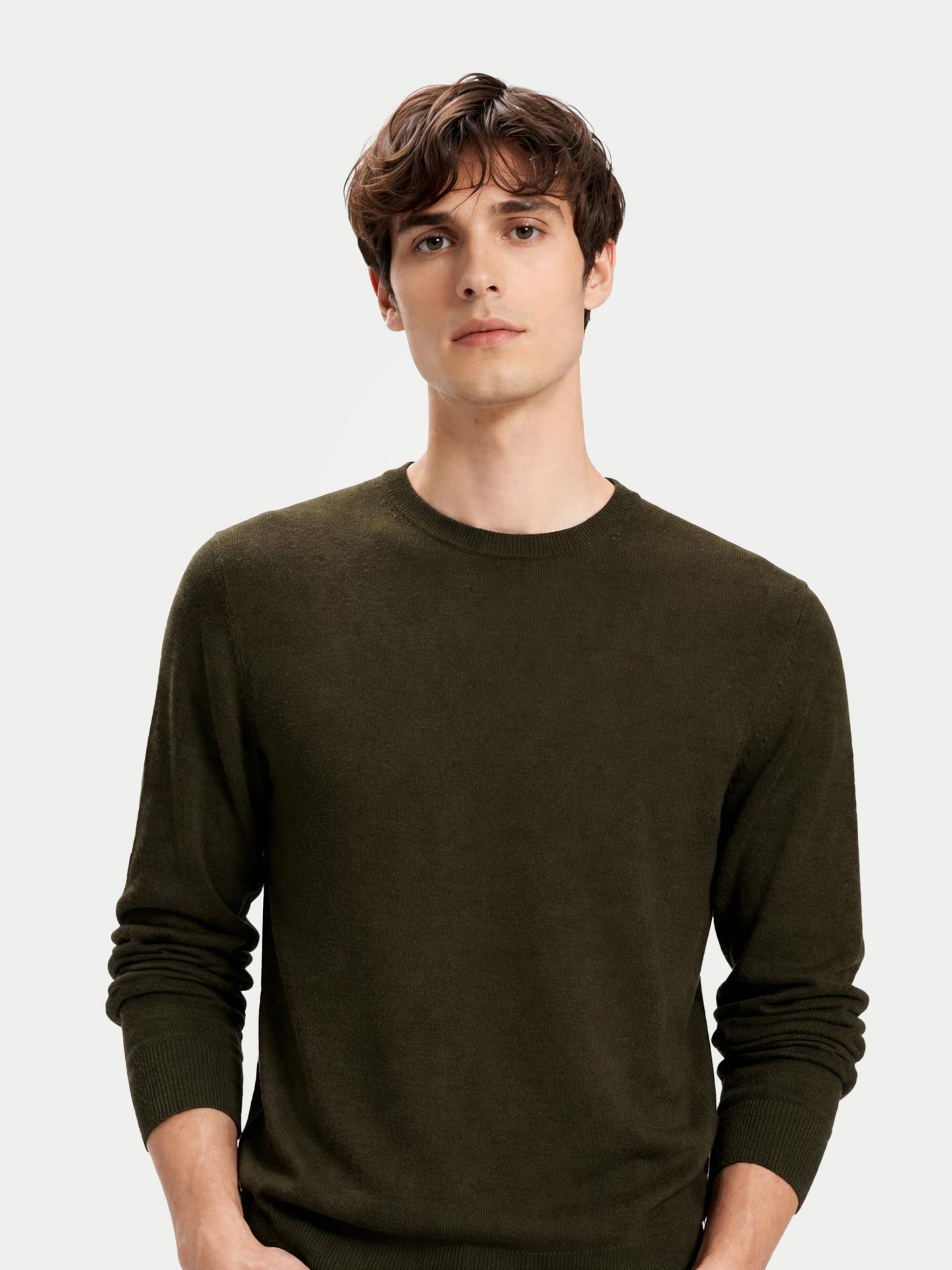 Gros plan de face d'un homme portant un pull ras du cou vert foncé sur fond gris clair.  #color_avocado