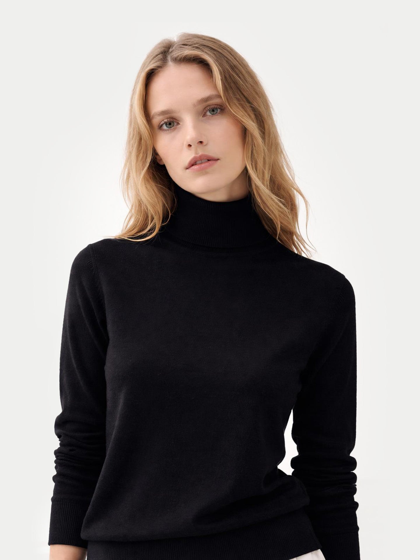 Gros plan de face d'une femme portant un pull à col roulé noir sur fond gris clair. #color_noir