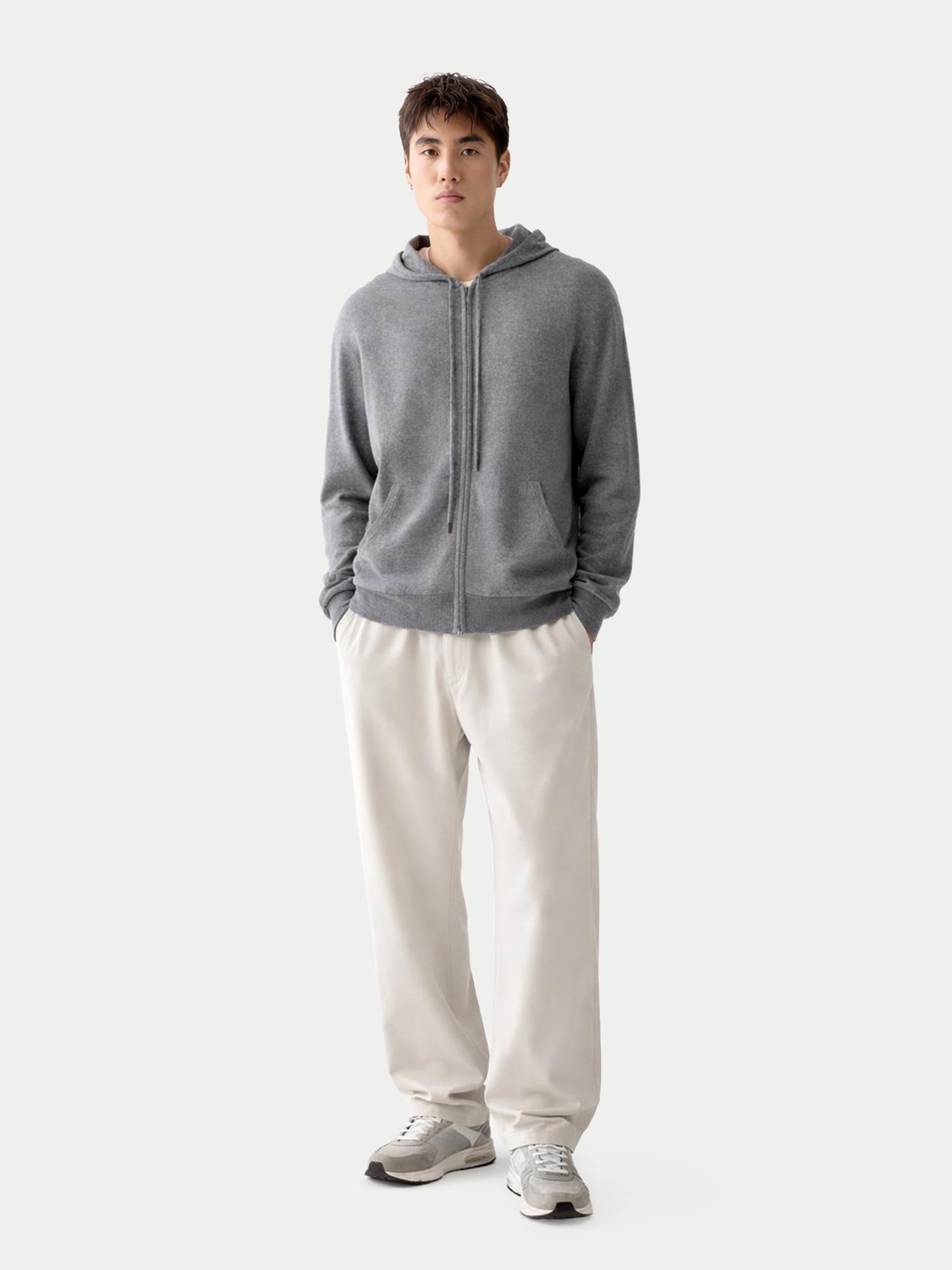 Vue de face d'un sweat à capuche gris zippé et d'un pantalon blanc sur fond gris clair. #color_gris-foncé