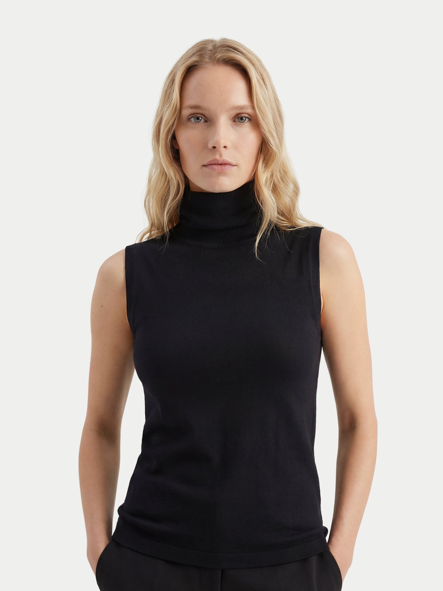 Gros plan de face d'une femme portant un haut en cachemire noir sans manches à col roulé assorti à un pantalon, sur un fond gris clair. #color_noir