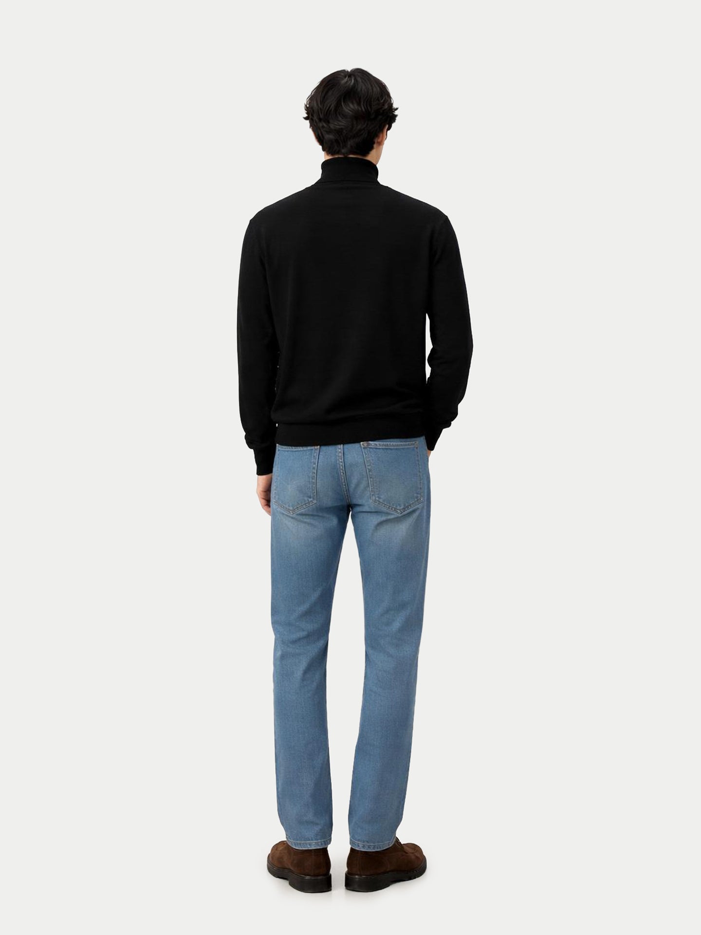 Vue de dos d'un homme debout, portant un pull à col roulé noir et un jean bleu, sur fond gris clair. #color_noir