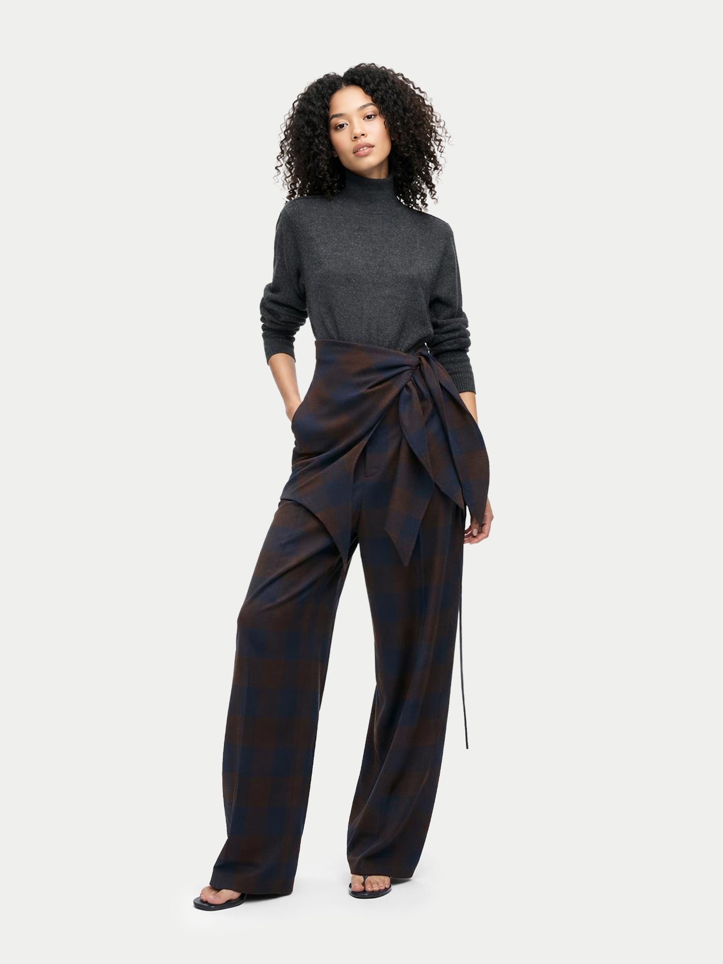 Vue de face d'une femme portant un pull à col montant foncé, une écharpe à carreaux marron nouée à la taille et un pantalon assorti. #couleur_gris-taupe