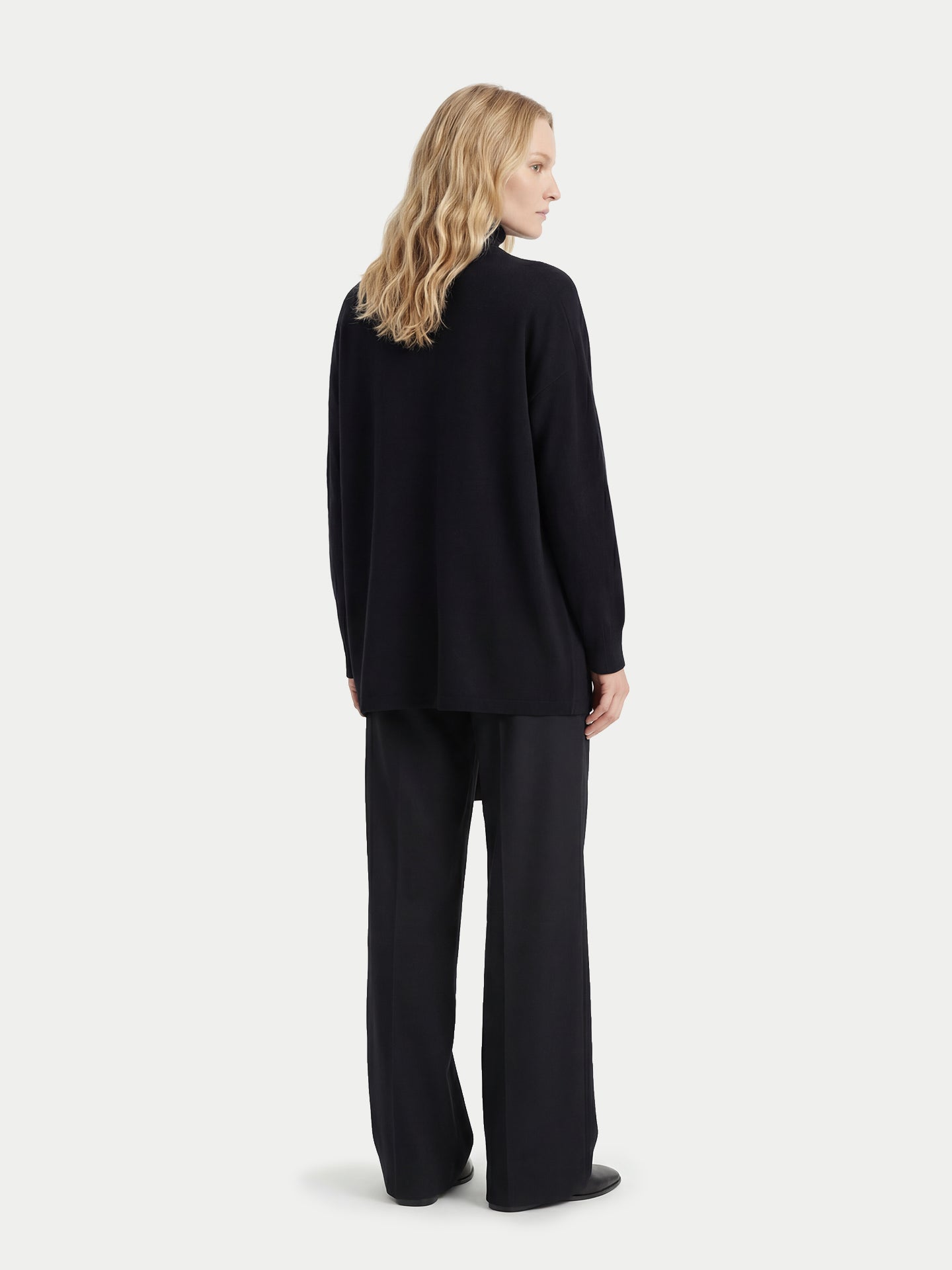 Vue de dos d'une femme portant un cardigan noir ouvert assorti à un pantalon, sur fond gris clair. #color_noir