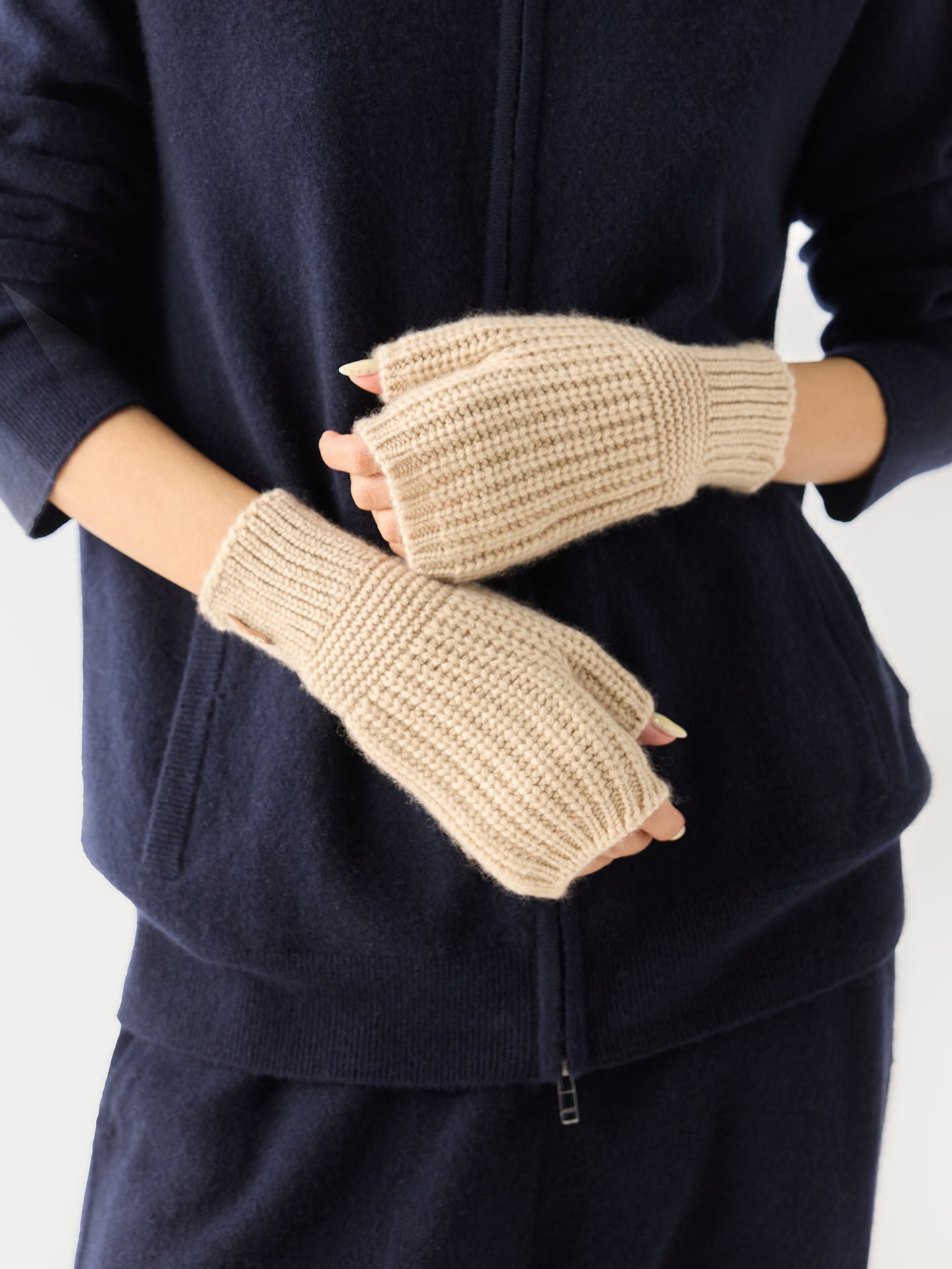 Gros plan de face d'une femme portant un ensemble bleu marine et des gants beiges sans doigts sur un fond gris clair. #color_beige