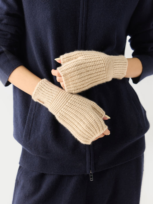 Gros plan de face d'une femme portant un ensemble bleu marine et des gants beiges sans doigts sur un fond gris clair. #color_beige