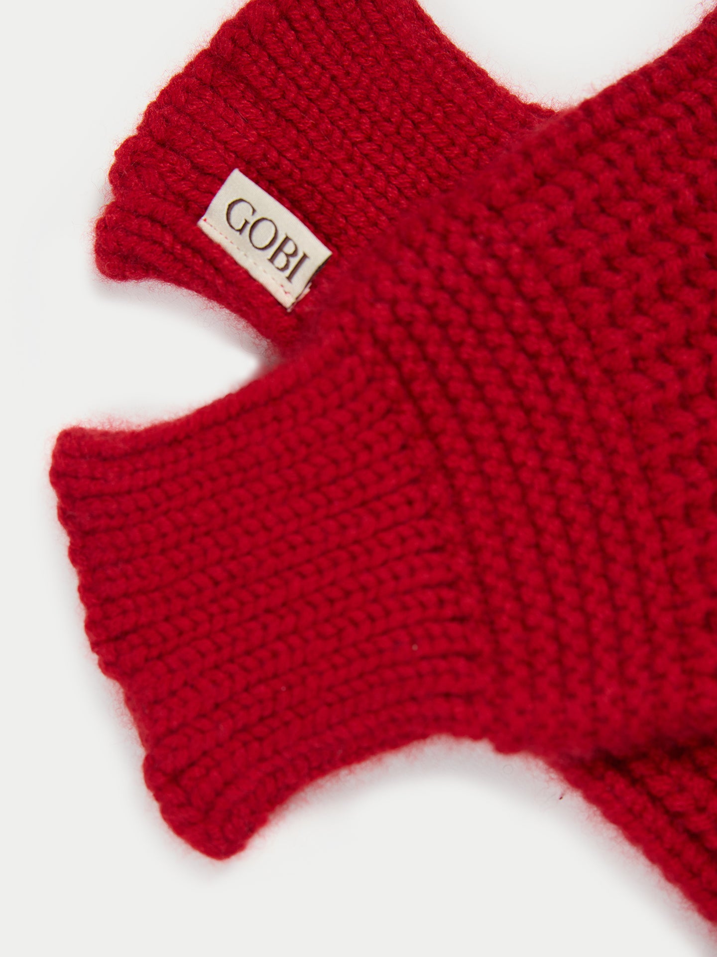 Gros plan sur des gants rouges sans doigts avec une petite étiquette de marque « GOBI » sur fond gris clair. #color_piment