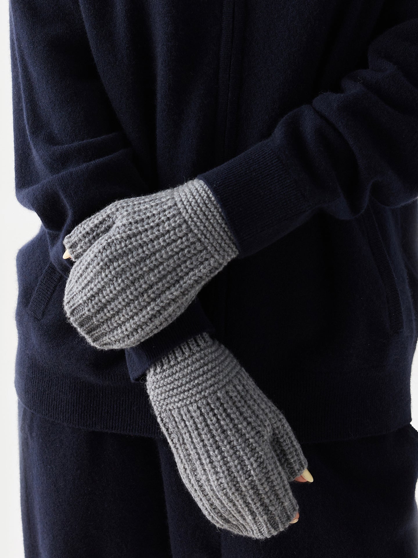 Gros plan de face d'une femme portant une tenue bleu marine et des gants gris sans doigts avec une petite étiquette de marque « GOBI » sur fond gris clair. #color_gris-foncé