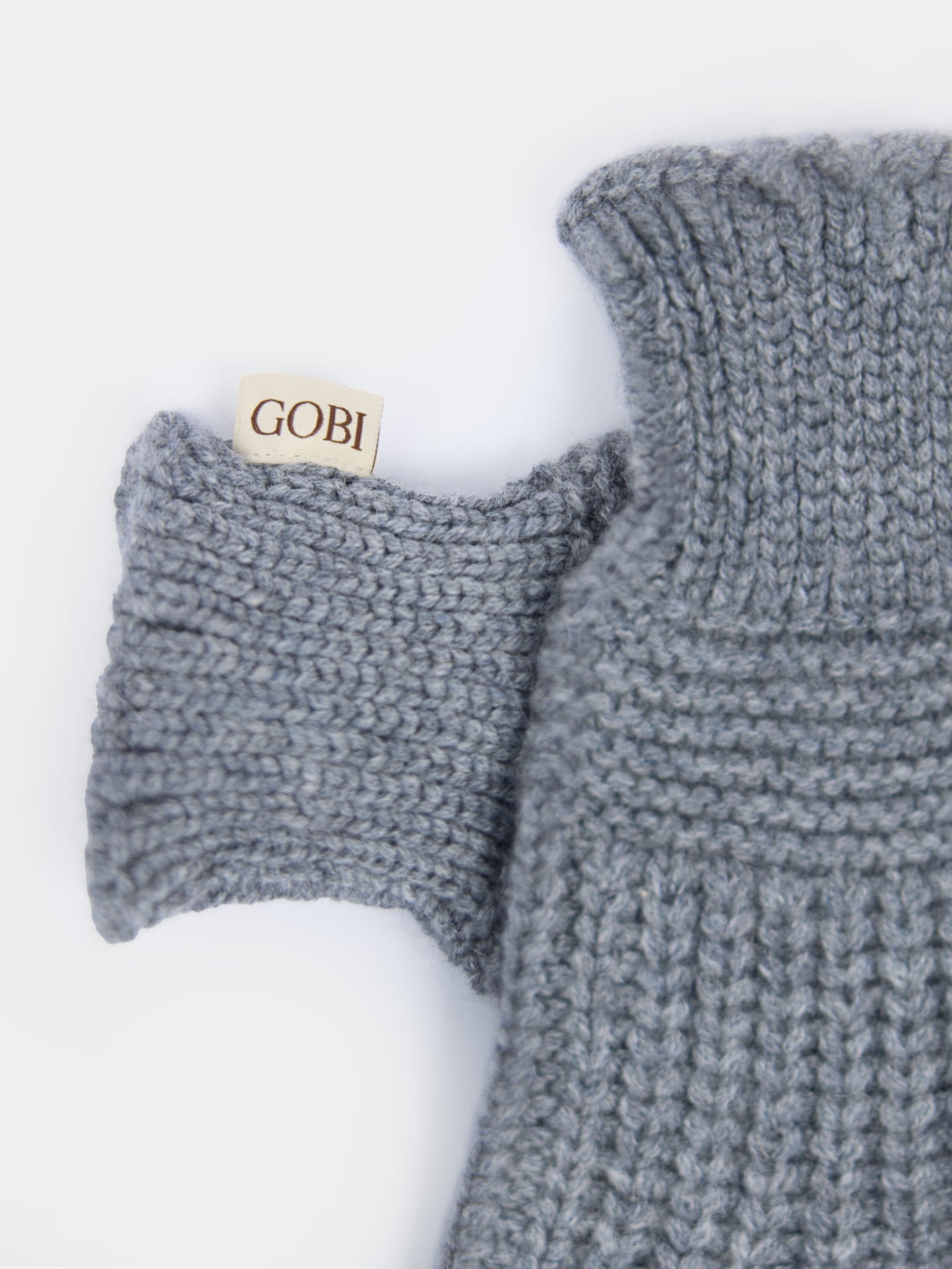 Gros plan sur des gants gris sans doigts avec une petite étiquette de marque « GOBI » sur fond gris clair. #color_gris-foncé