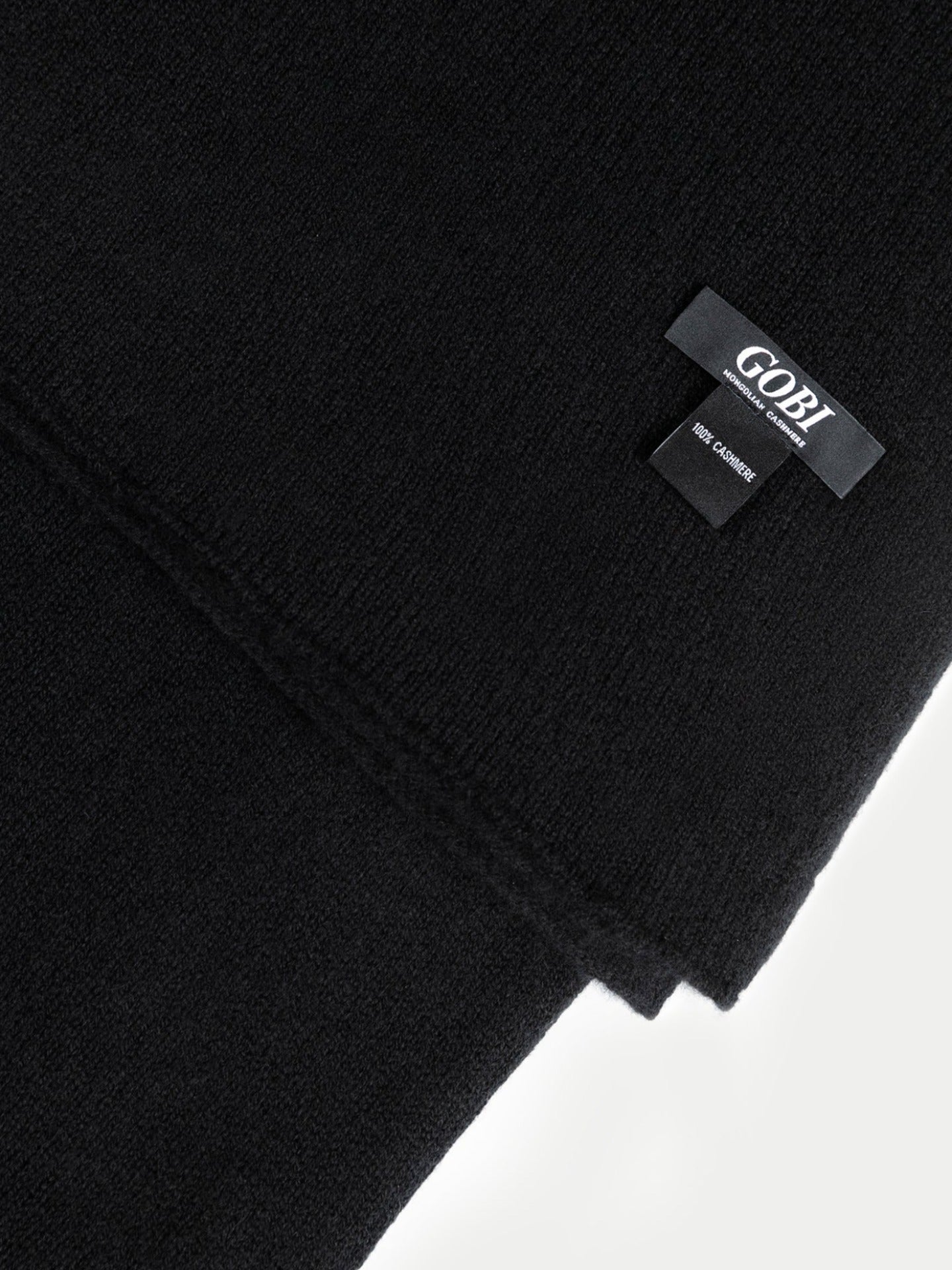 Gros plan sur une écharpe noire avec une petite étiquette de marque « GOBI », « 100 % cachemire », sur fond gris clair. #color_noir