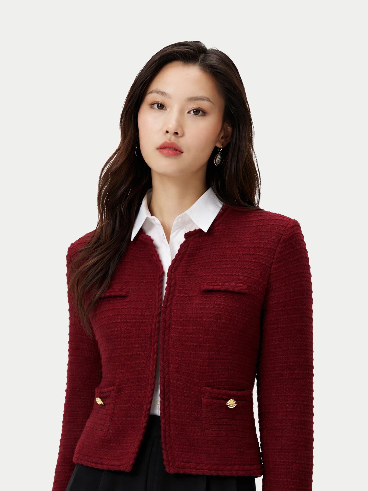 Vue de face d'une femme portant un cardigan bordeaux en maille à col rond et boutons dorés sur les poches latérales, par-dessus une chemise blanche et une jupe noire, sur fond gris clair. #color_Zindanfil