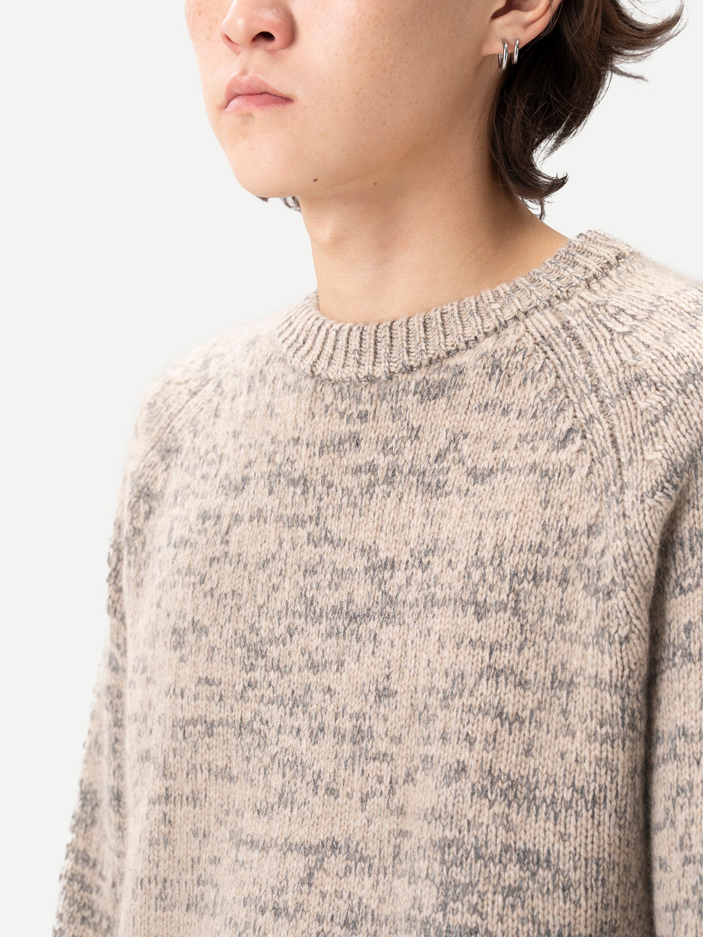 Gros plan sur un homme portant un pull à col rond côtelé beige-taupe sur fond gris clair. #color_oxfor-tan