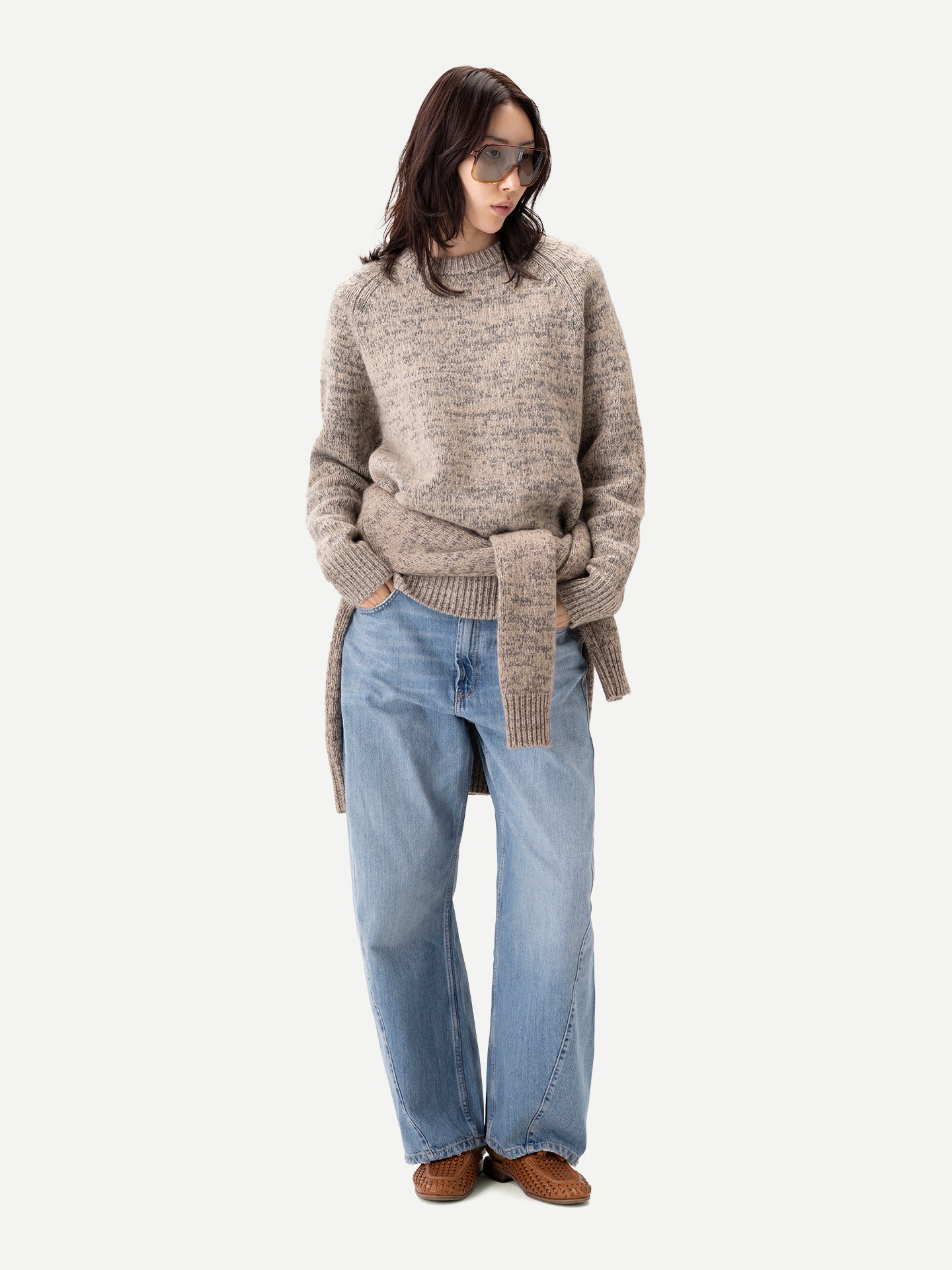 Vue de face d'une femme debout, portant un pull ras du cou beige-taupe noué à la taille, par-dessus un jean bleu, sur fond gris clair. #color_oxfor-tan