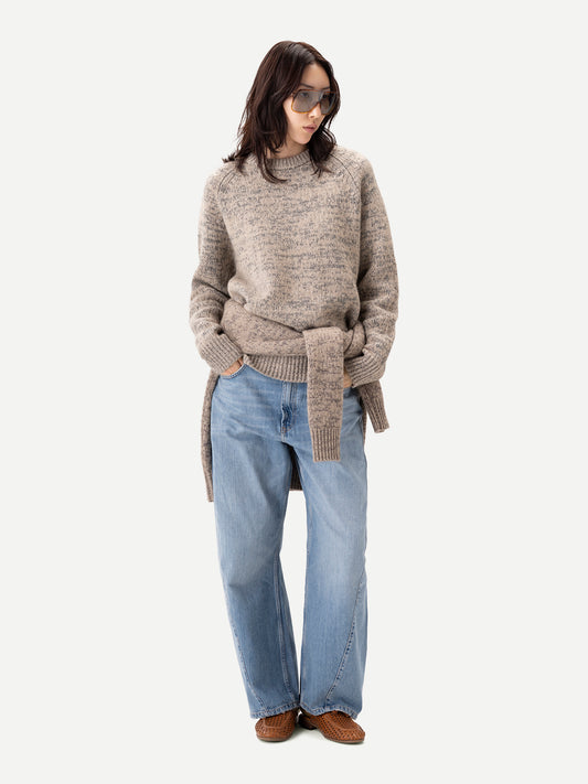 Vue de face d'une femme debout, portant un pull ras du cou beige-taupe noué à la taille, par-dessus un jean bleu, sur fond gris clair. #color_oxfor-tan