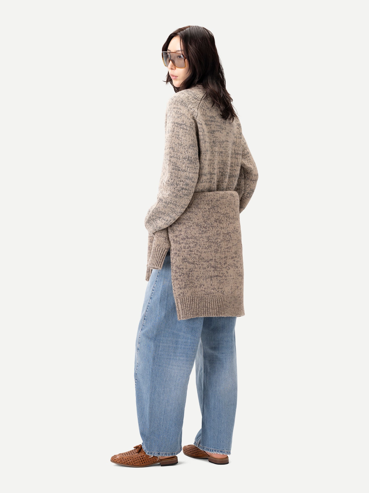 Vue de profil d'une femme debout, portant un pull ras du cou beige-taupe noué à la taille, par-dessus un jean bleu, sur fond gris clair. #color_oxfor-tan