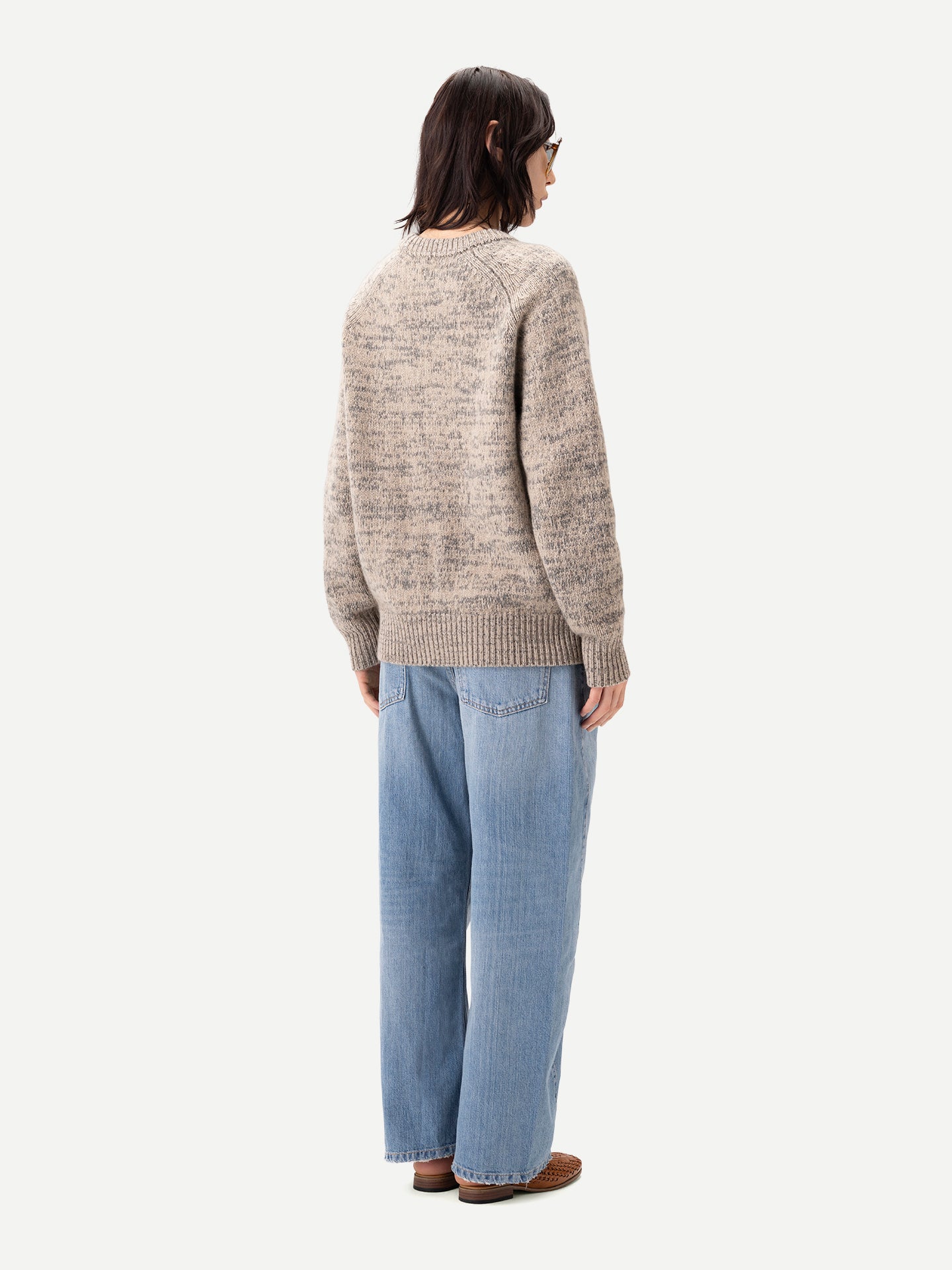Vue de dos d'une femme debout, portant un pull ras du cou beige-taupe et un jean bleu, sur fond gris clair. #color_oxfor-tan