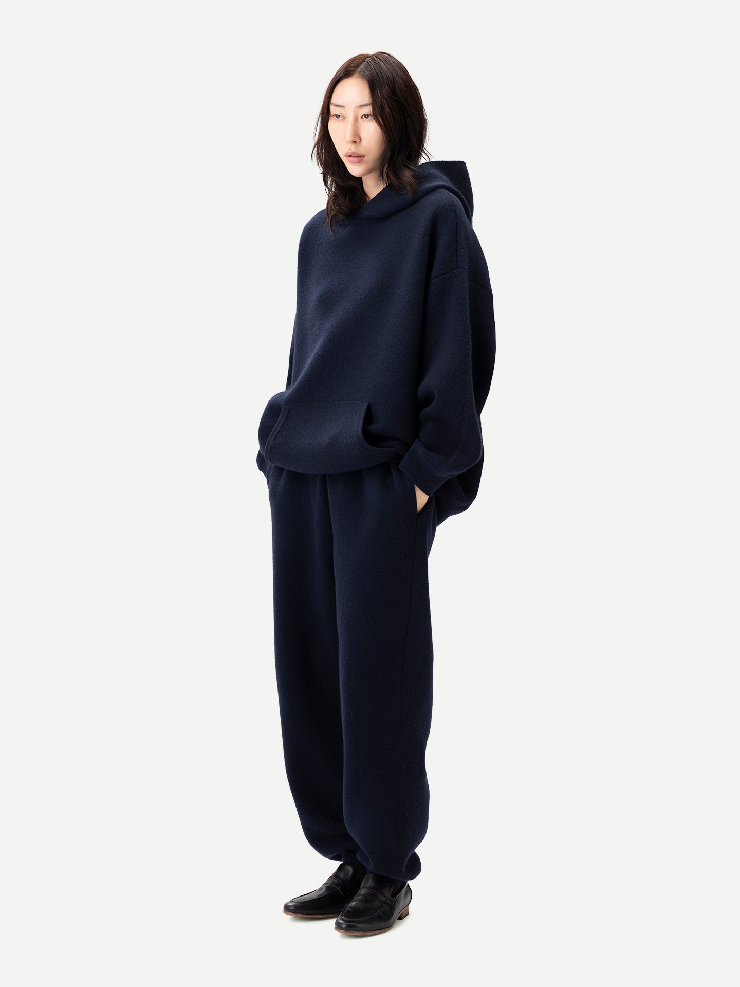 Vue de profil d'une femme portant un ensemble bleu marine composé d'un sweat à capuche à poche et d'un pantalon de jogging, sur fond gris clair. #color_india-ink