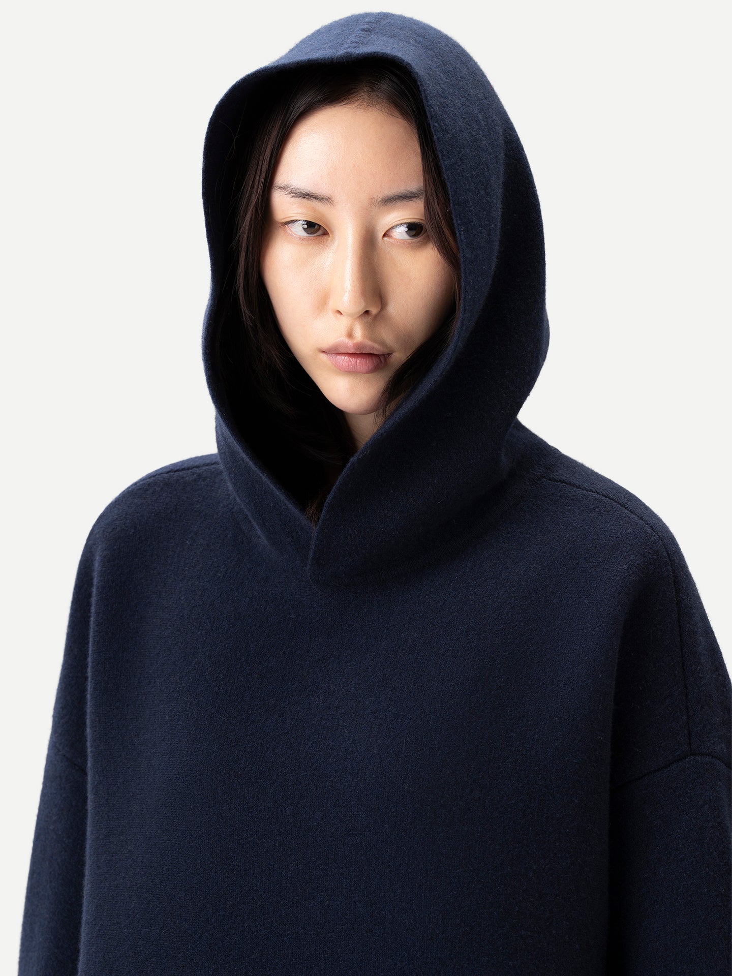 Gros plan de face d'une femme debout, capuche relevée, portant un sweat-shirt bleu marine, sur fond gris clair. #color_india-ink