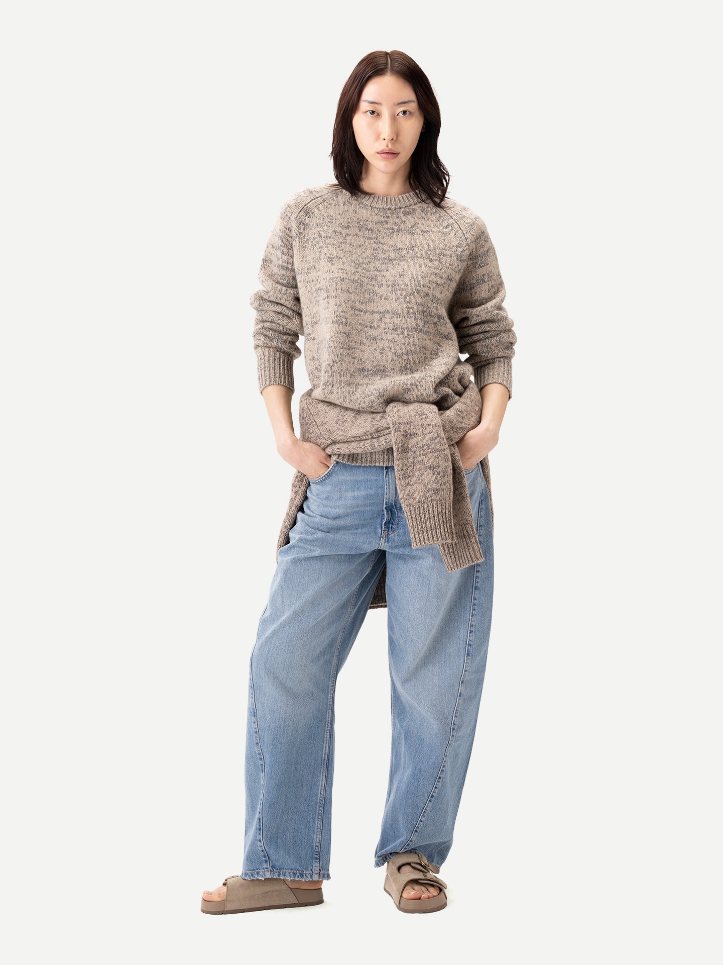 Vue de face d'une personne debout portant un pull ras du cou beige-taupe chiné, noué à la taille, sur un jean bleu, sur fond gris clair. #color_oxfor-tan