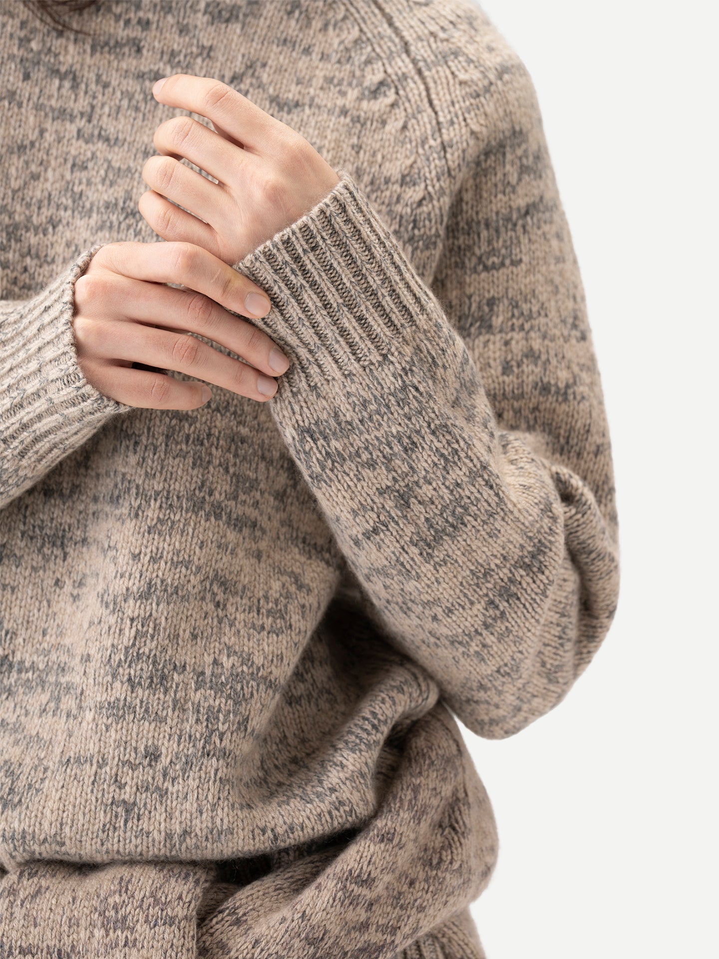 Gros plan de face d'un pull beige-taupe chiné à poignets côtelés sur fond gris clair. #color_oxfor-tan