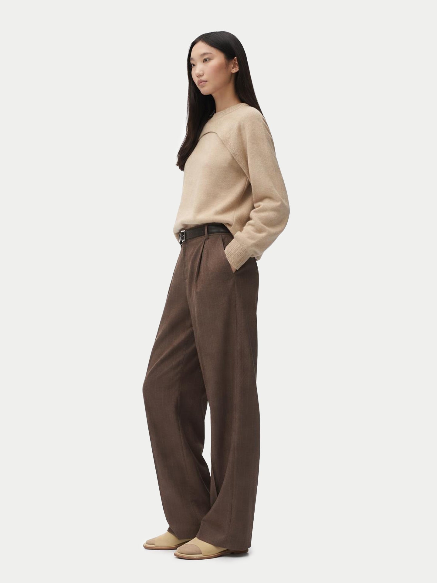 Vue de face d'une femme portant un pull beige en maille à motif architectural avec un empiècement sur la poitrine, associé à un pantalon en laine à fines rayures et une ceinture noire. #color_gris-chaud