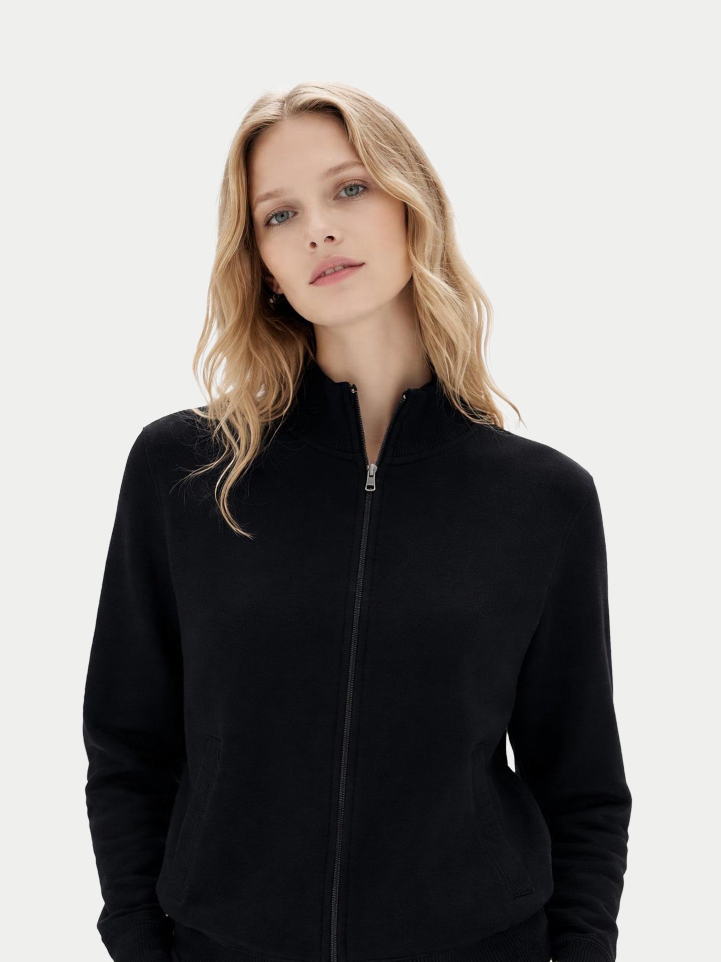 Gros plan de face d'une femme portant un cardigan noir zippé à poches latérales sur fond gris clair. #color_noir