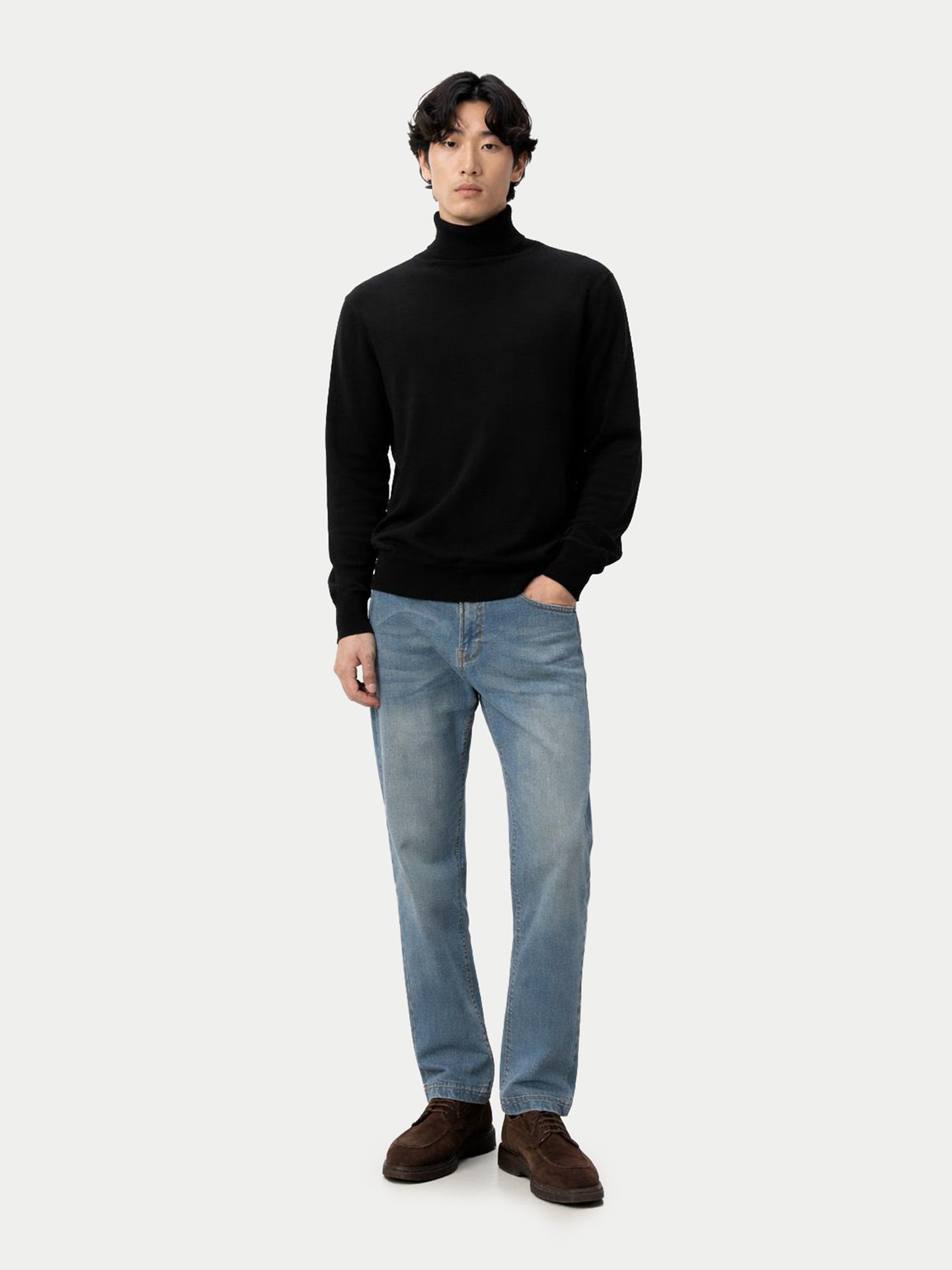 Vue de face d'un homme debout, portant un pull à col roulé noir et un jean bleu, sur fond gris clair. #color_noir
