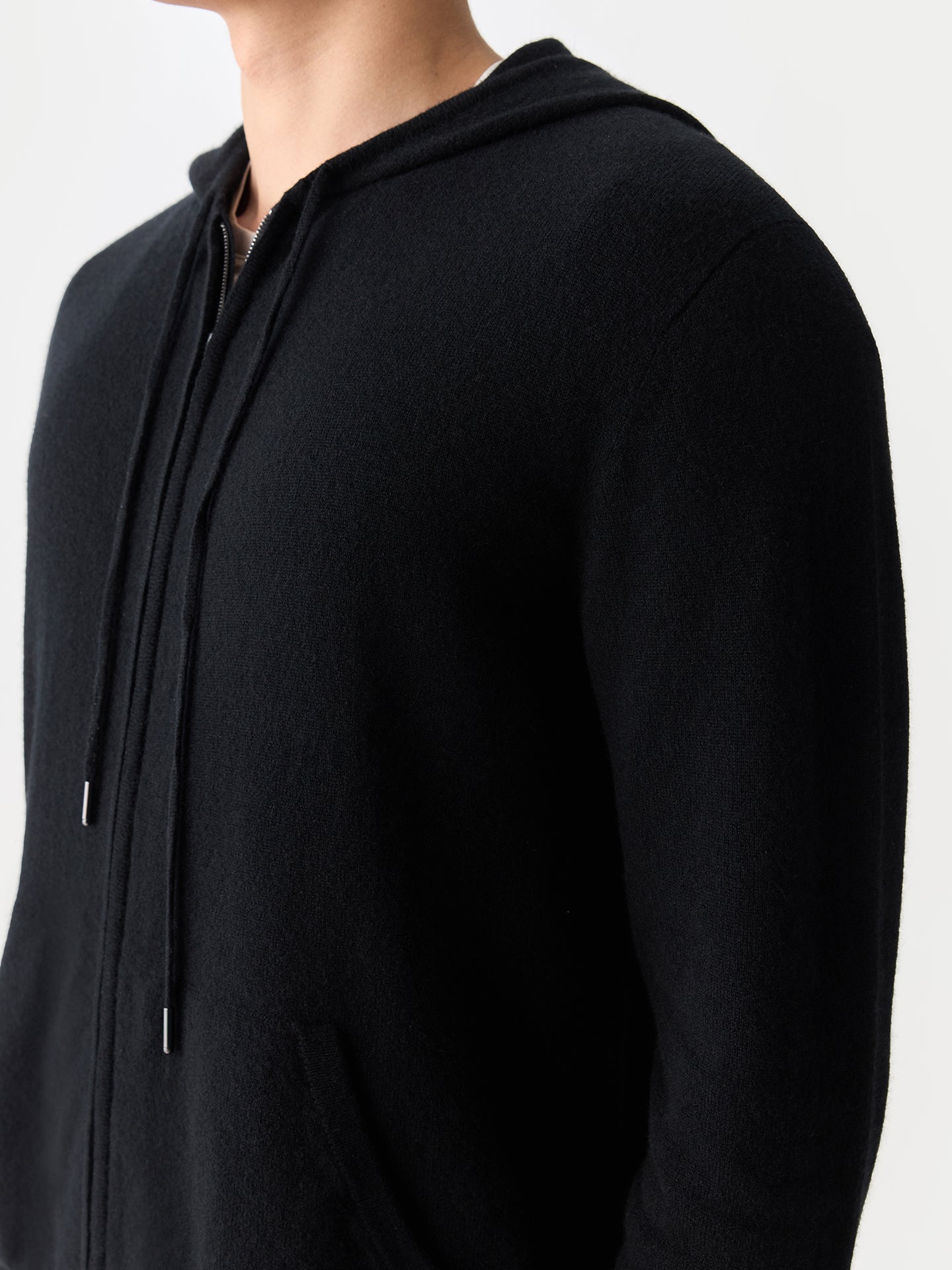 Gros plan de profil d'un homme portant un sweat à capuche noir zippé sur fond gris clair. #color_noir