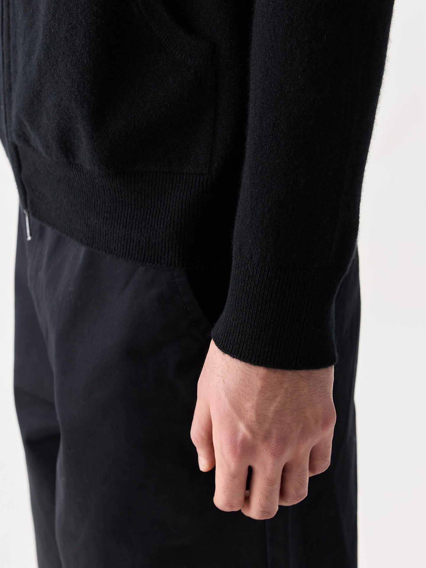 Gros plan de profil d'un homme portant un sweat à capuche noir (détail sur la manche) et un pantalon noir sur fond gris clair. #color_noir