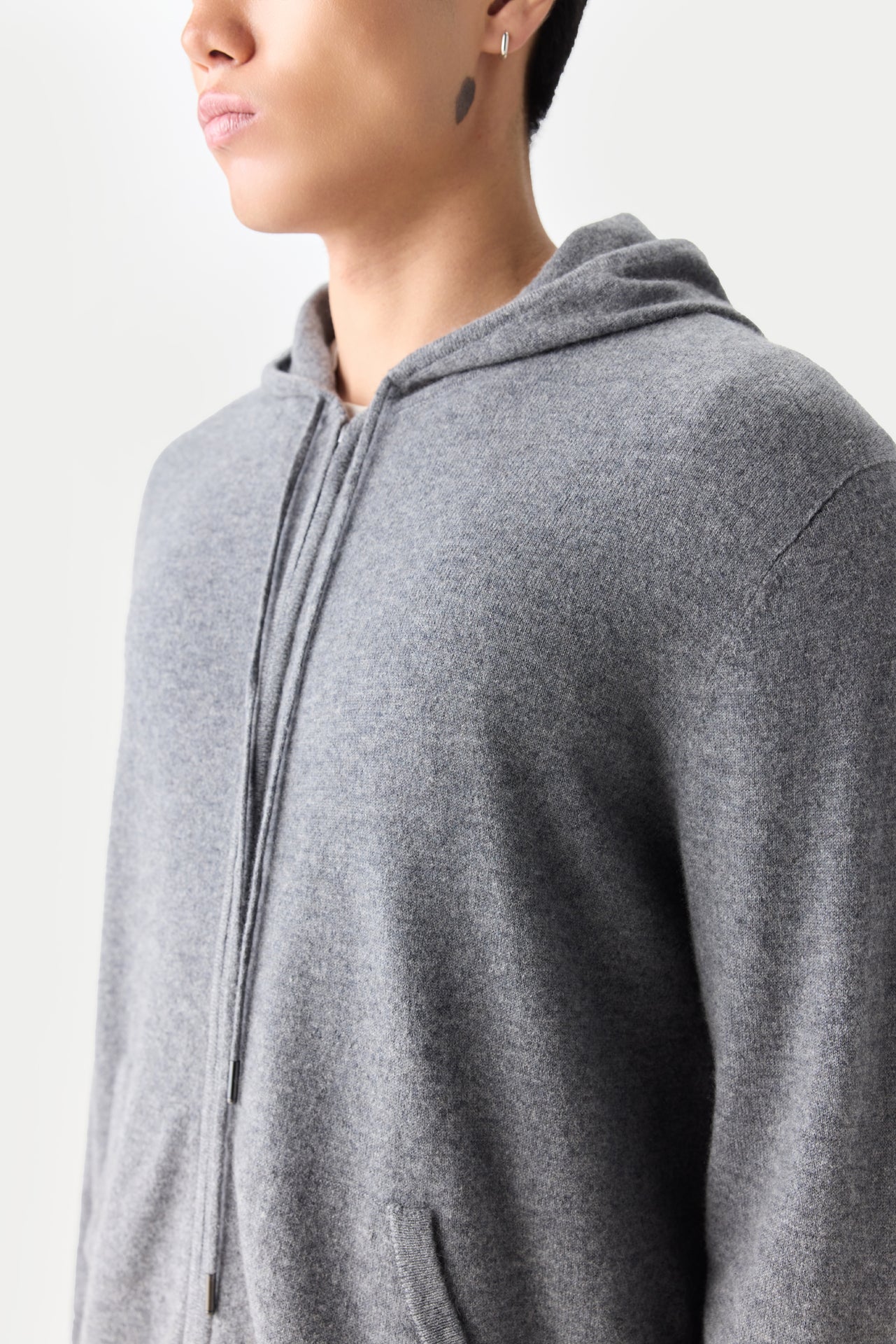 Gros plan latéral d'un sweat à capuche gris zippé sur fond gris clair. #color_gris-foncé