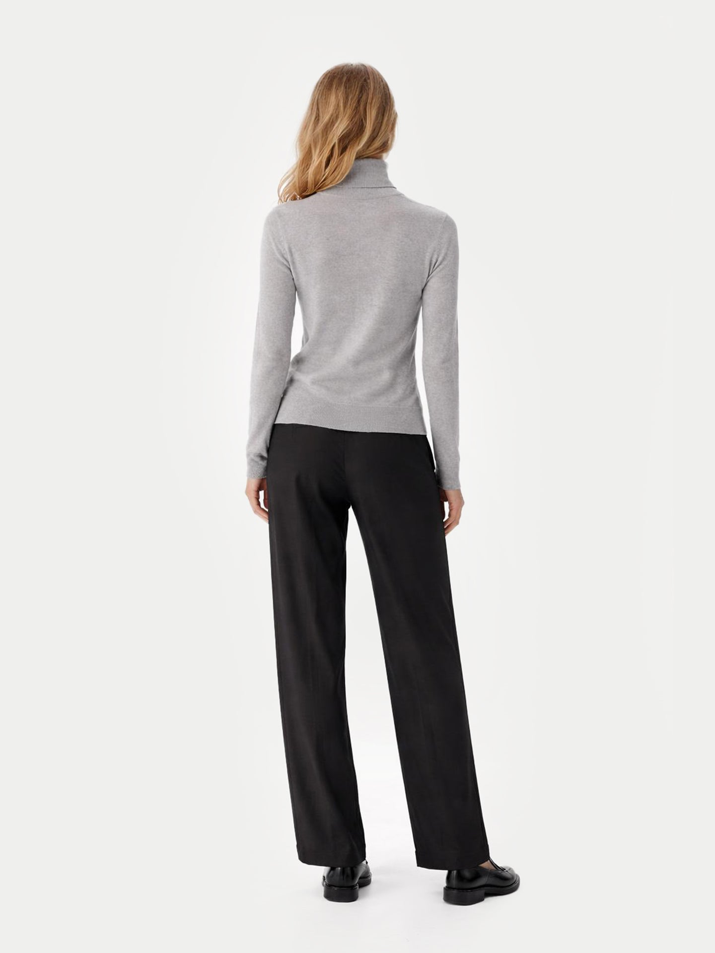 Vue de dos d'une femme portant un pull à col roulé gris et un pantalon noir sur fond gris clair. #color_high-rise