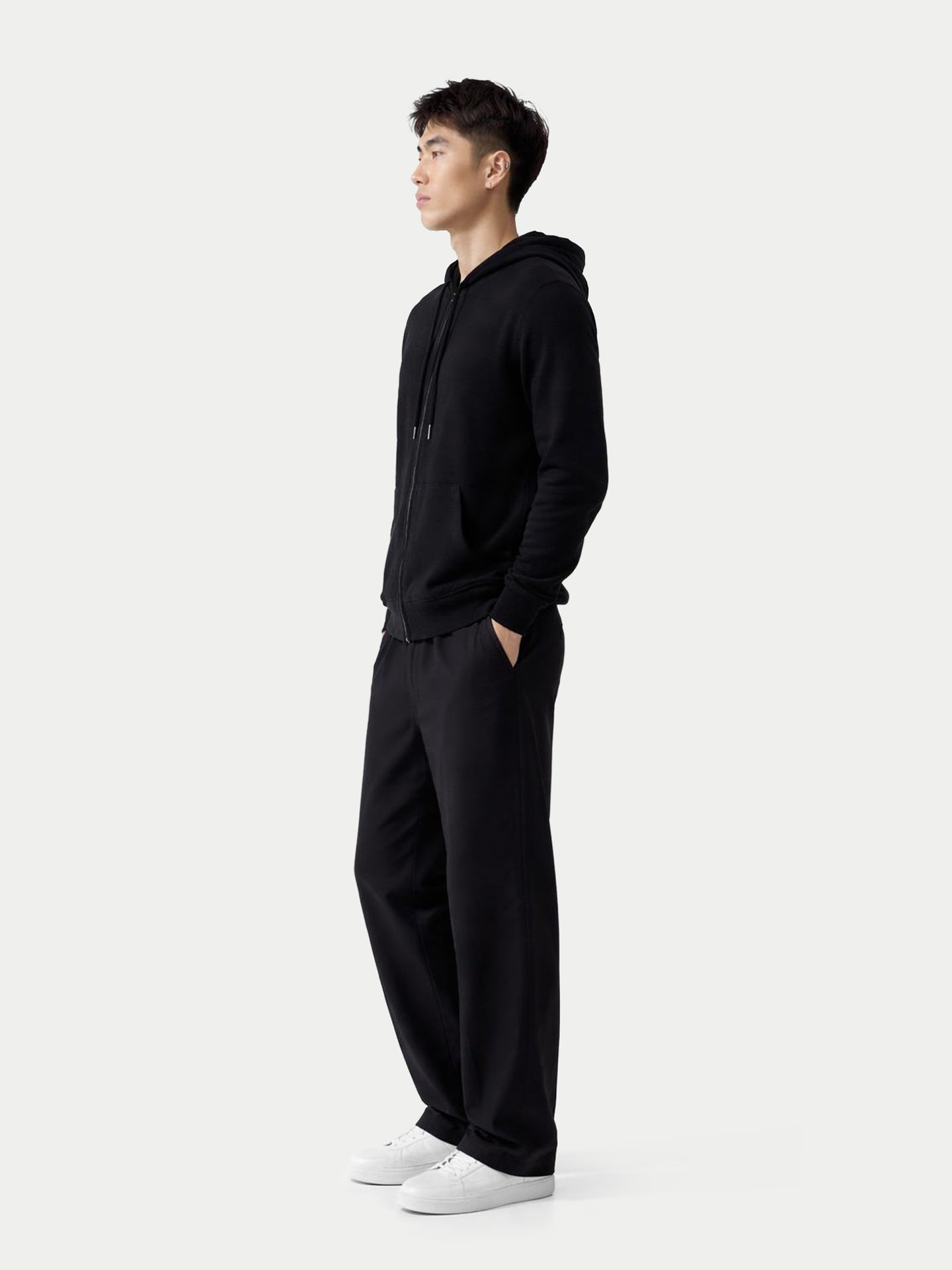 Vue de profil d'un homme portant un sweat à capuche noir zippé et un pantalon sur fond gris clair. #color_noir