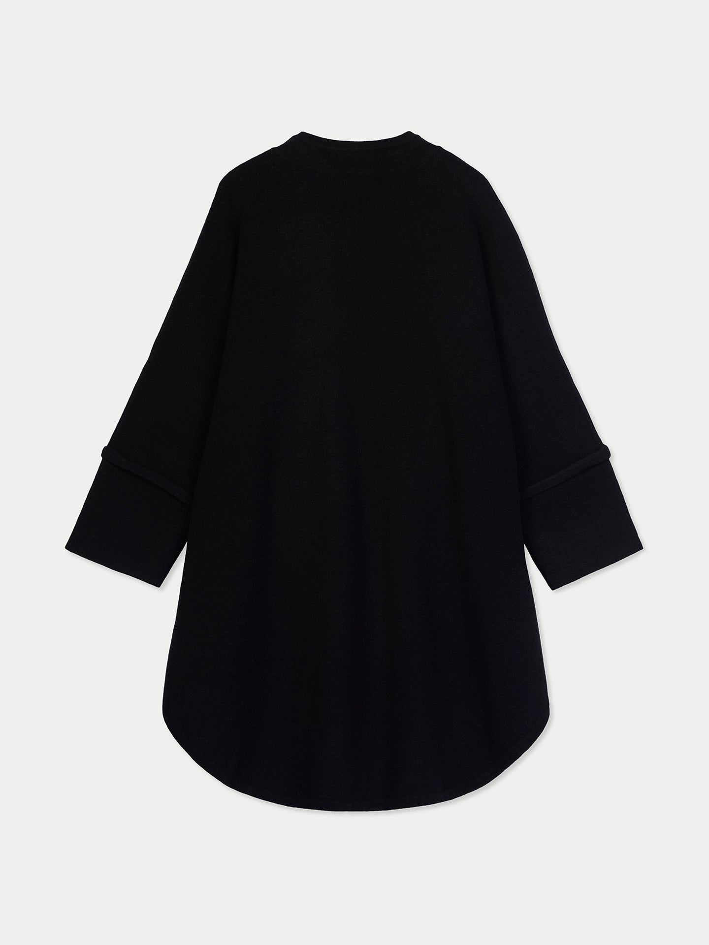 Vue de dos d'une femme portant un long poncho noir et un pantalon blanc sur fond blanc. #color_blanc
