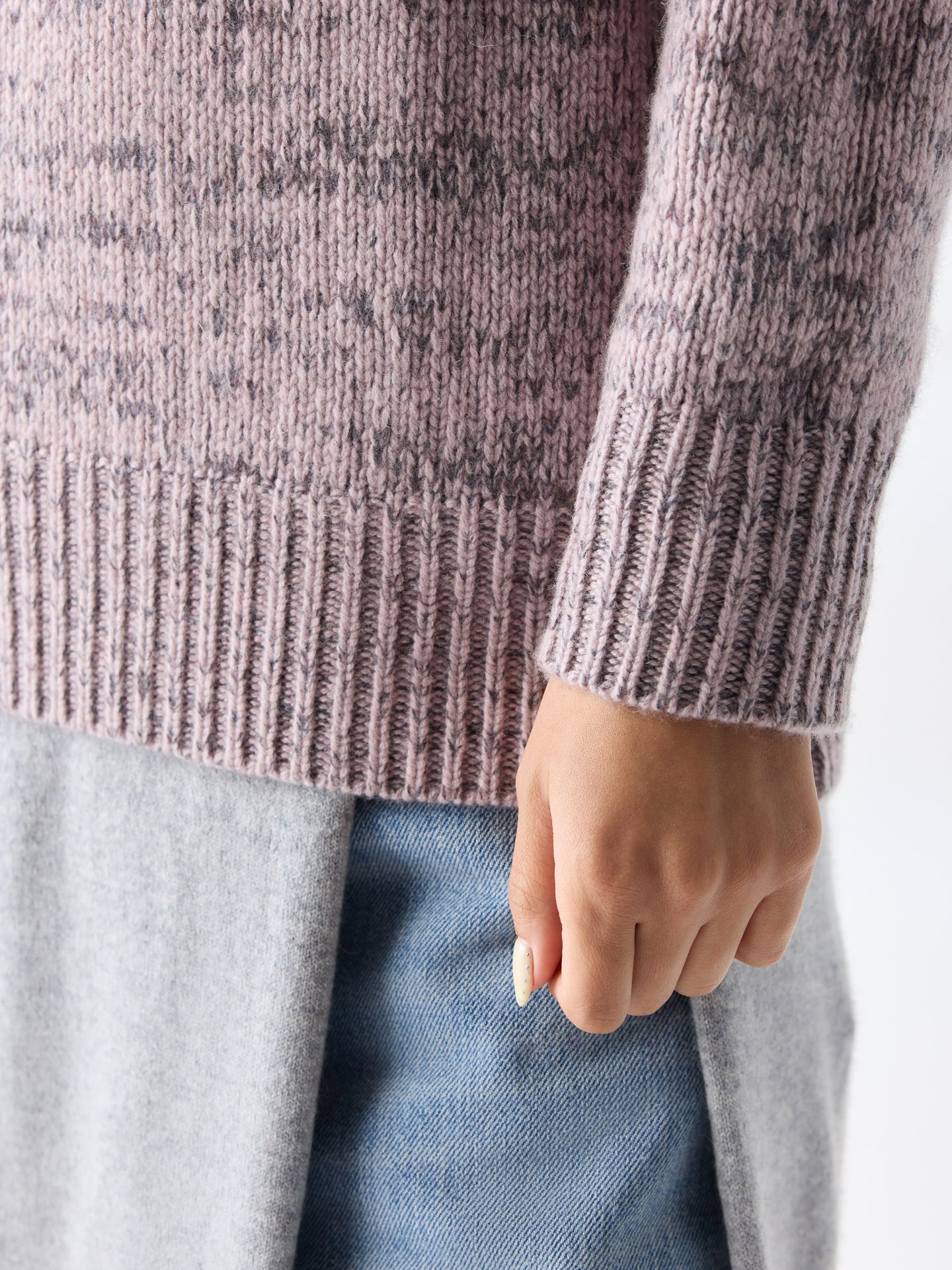 Gros plan sur un pull à poignets côtelés rose-gris chiné sur fond gris clair. #color_rose-ivoire