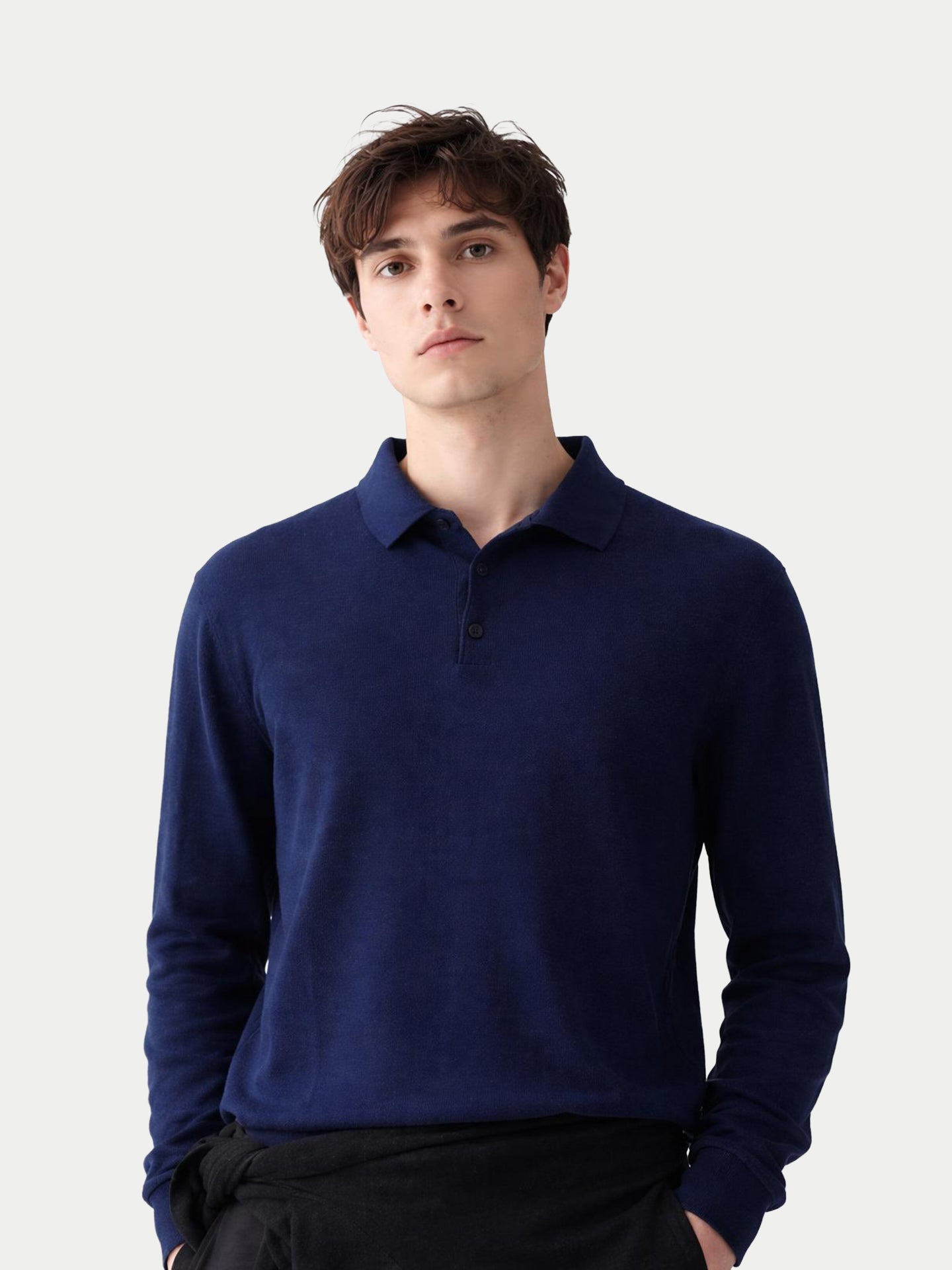 Gros plan de face d'un homme portant un polo bleu marine à manches longues sur fond gris clair. #color_mood-indigo