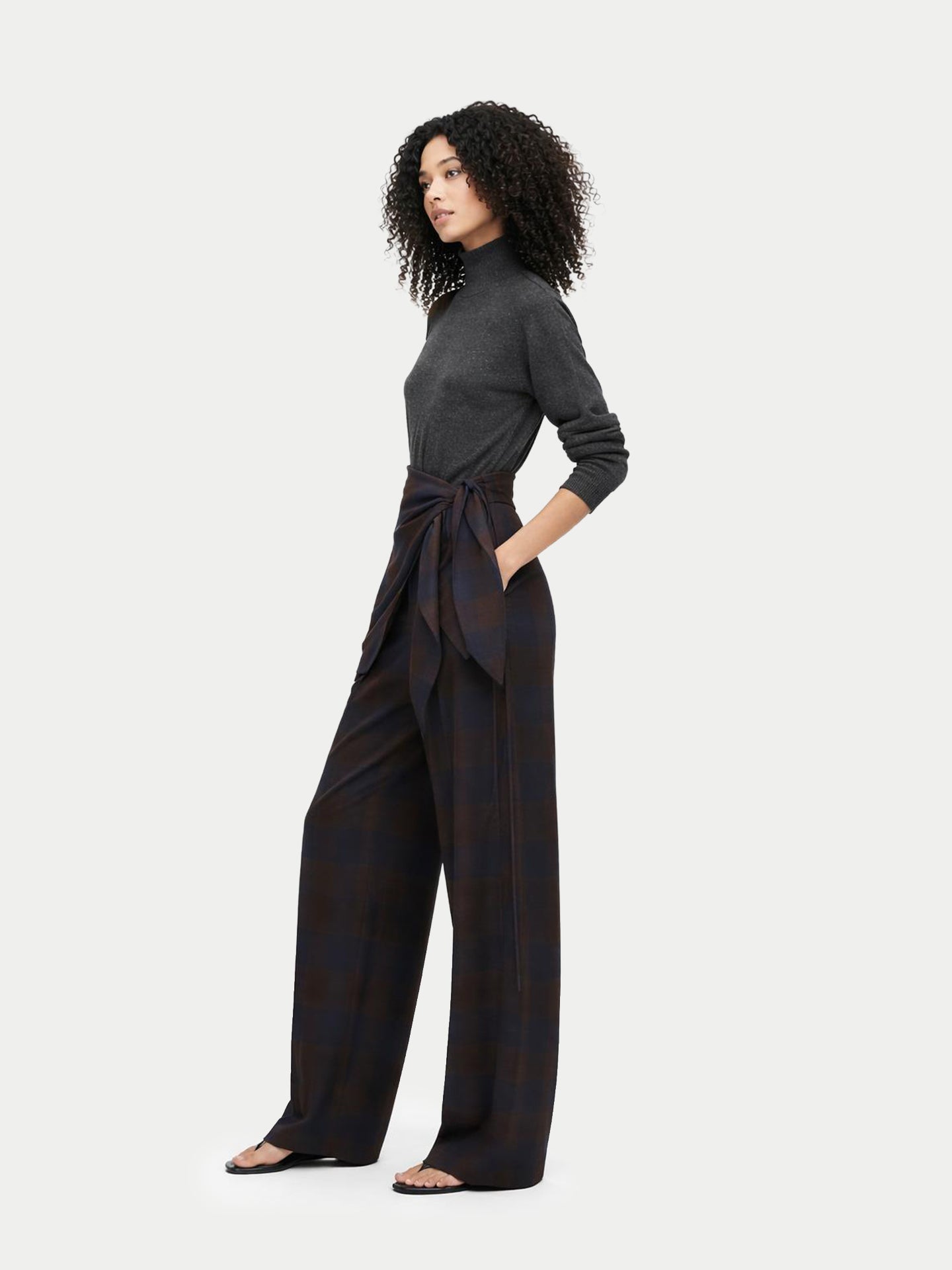 Vue de profil d'une femme portant un pull à col montant foncé, une écharpe à carreaux marron nouée à la taille et un pantalon assorti. #color_gris-taupe