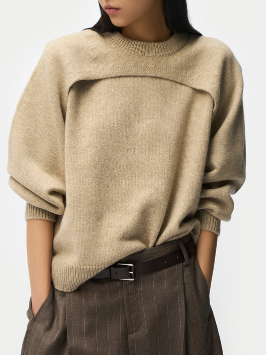 Gros plan sur un pull beige en maille architecturale avec empiècement poitrine, porté avec un pantalon en laine à fines rayures et une ceinture noire. #color_gris-chaud