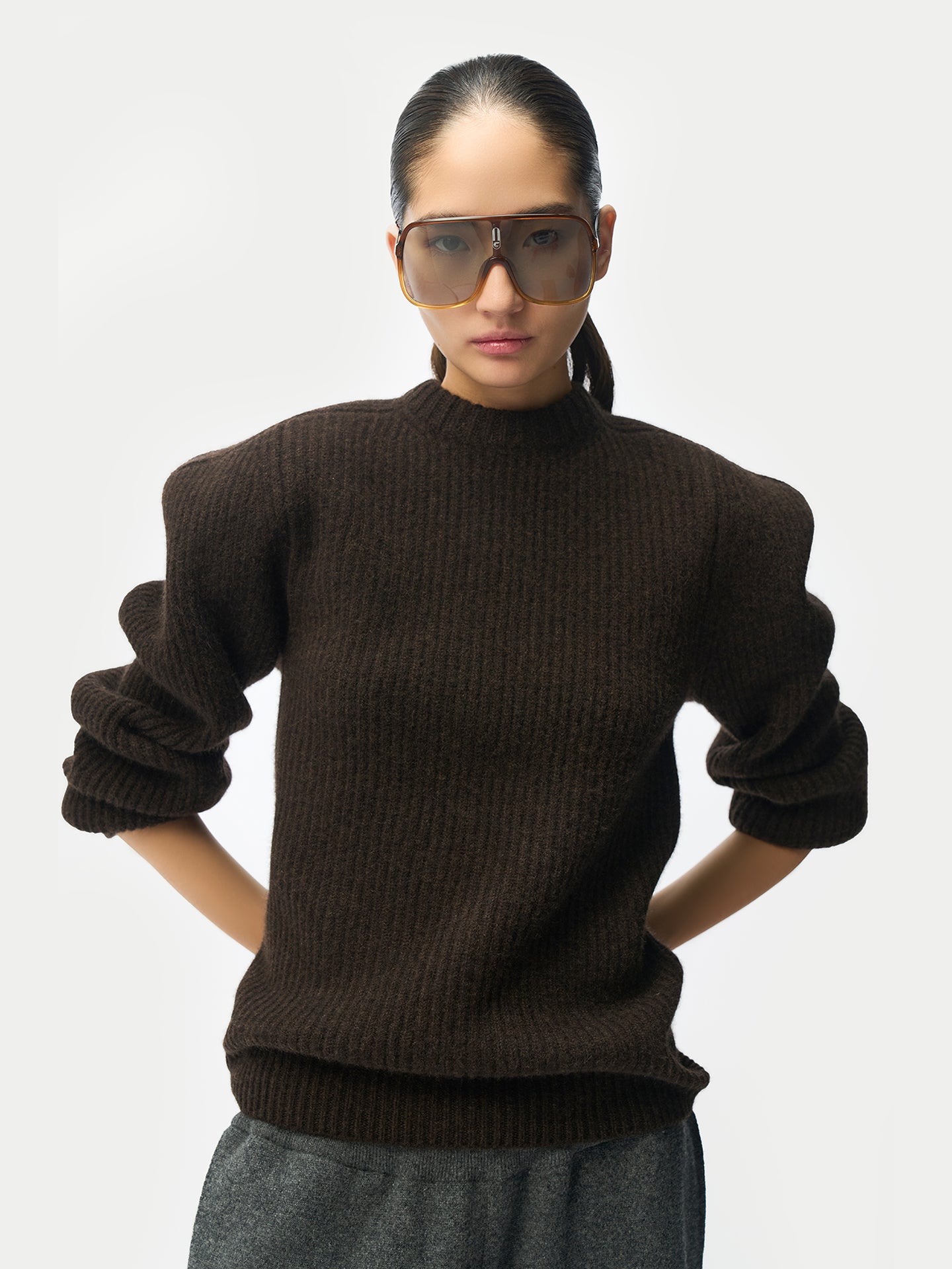 Gros plan de face d'une femme portant un pull côtelé marron sculpté sur fond gris clair. #color_mole