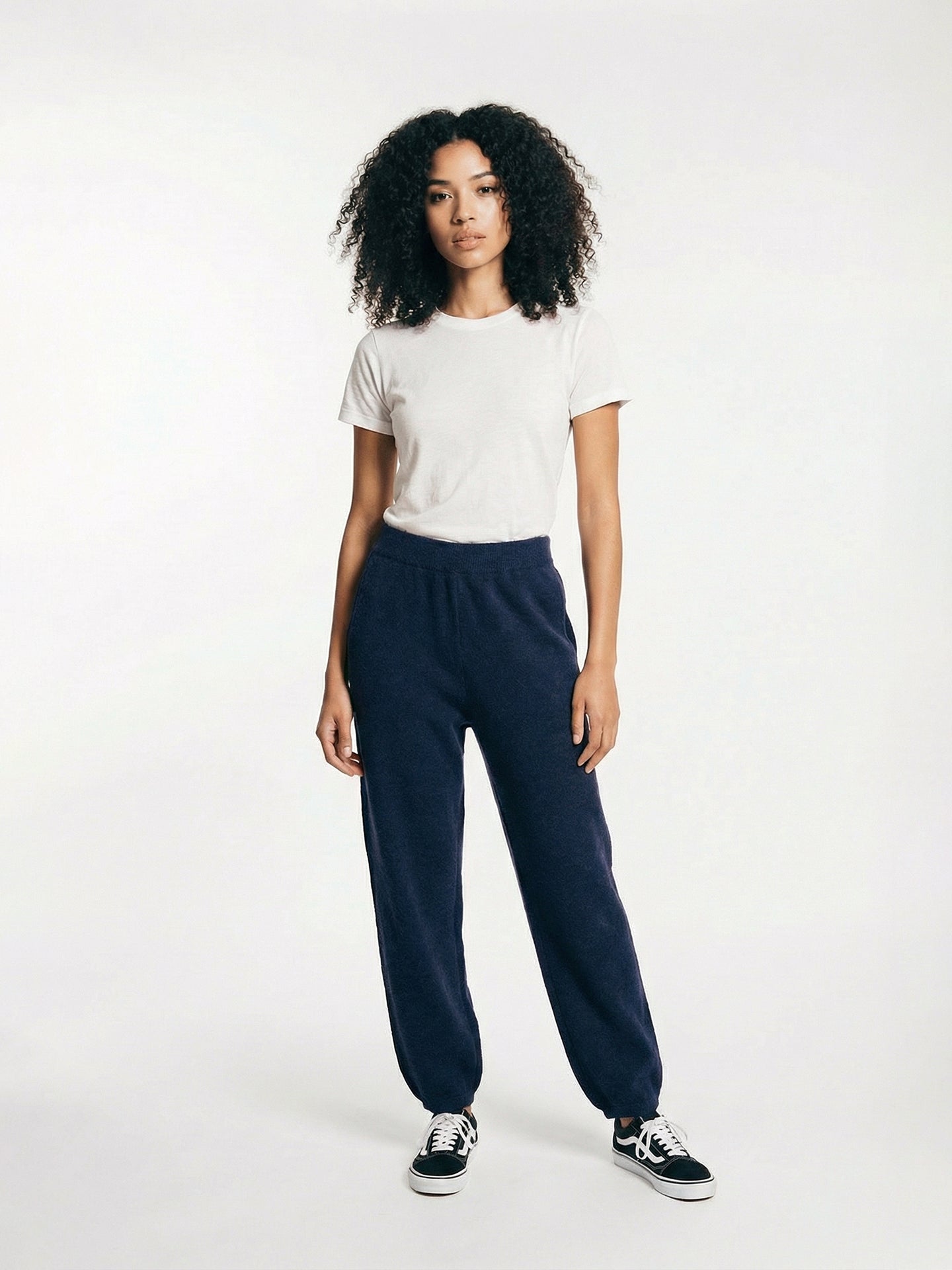 Vue de face d'une femme portant un pantalon de jogging bleu marine et une chemise blanche sur fond gris clair. #color_india-ink